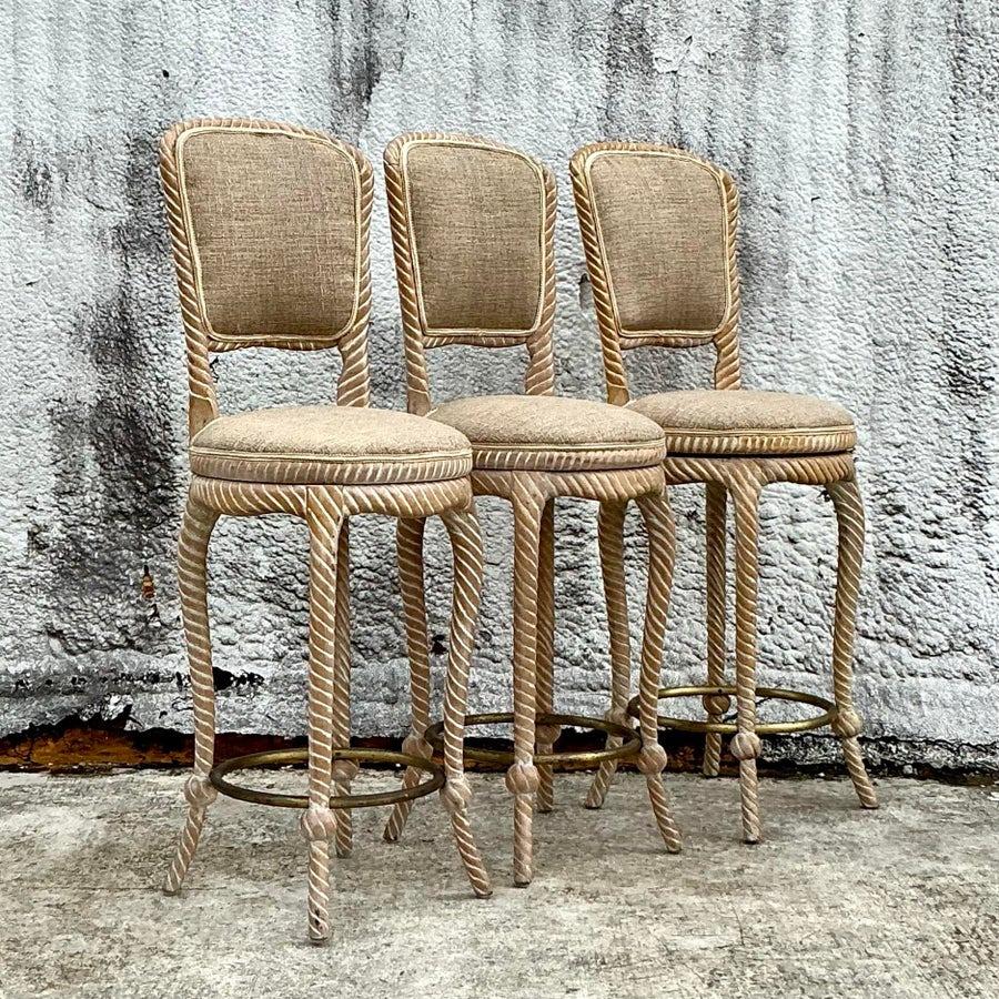 Add timeless elegance to your space with this exquisite set of three vintage Regency-style swivel bar stools. Featuring intricately carved rope-inspired frames with a chic cerused finish, these stools bring a unique blend of sophistication and
