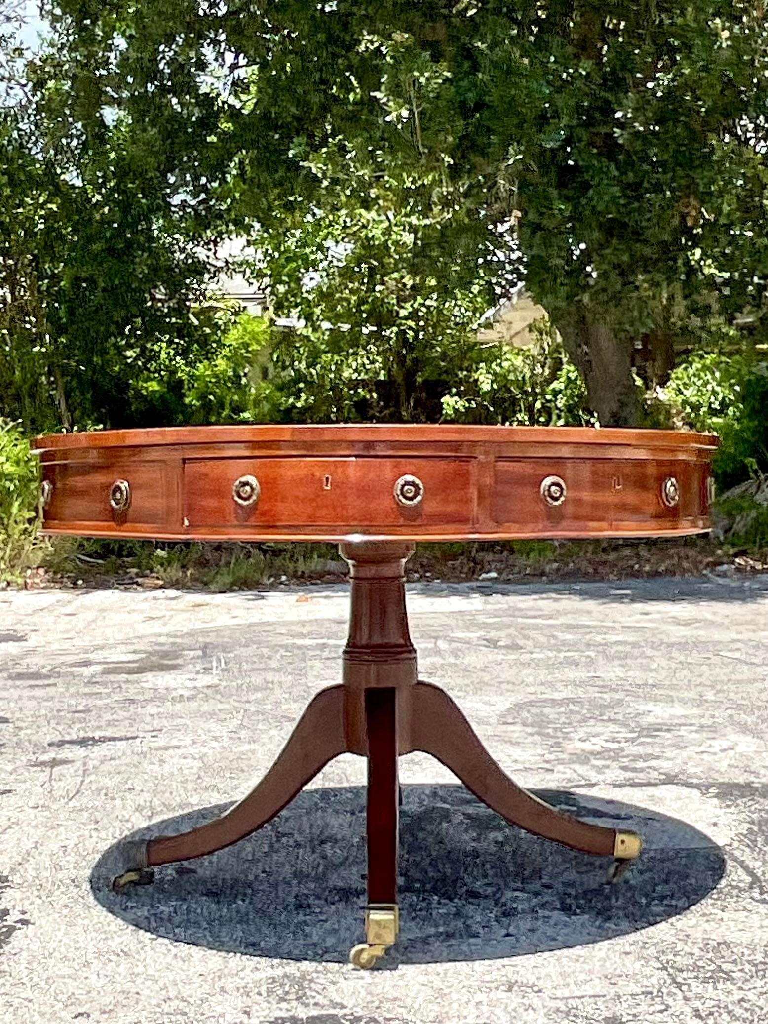 An exceptional vintage Regency center hall table. A chic circa 1850 drum top table with four working drawers and four faux drawers. A gorgeous hand embossed leather top. A center hand turned pedestal with four longs in brass box casters. Acquired