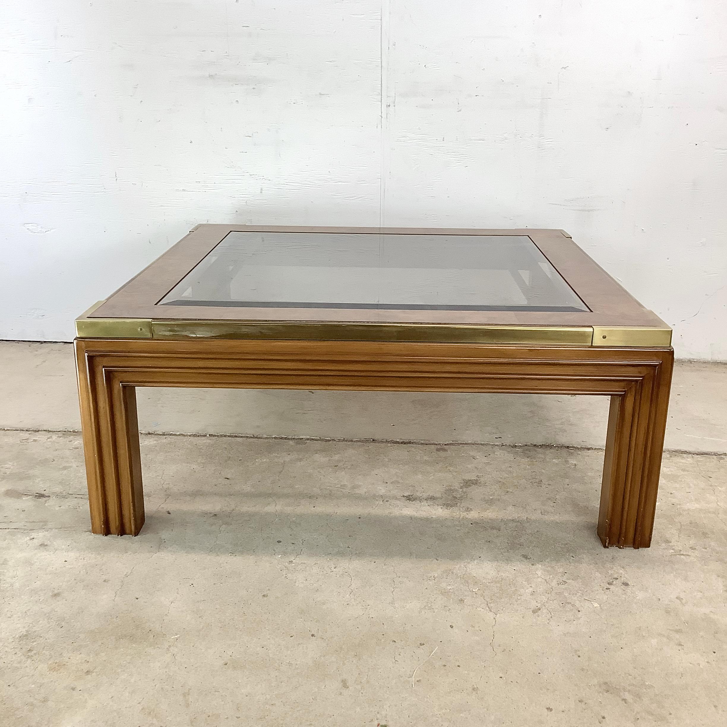 A beautifully preserved square vintage coffee table from the 1970s, showcasing an elevated blend of materials and timeless form. This piece features a smoked glass inset top, framed in highly figured burled wood veneer with subtle but striking brass
