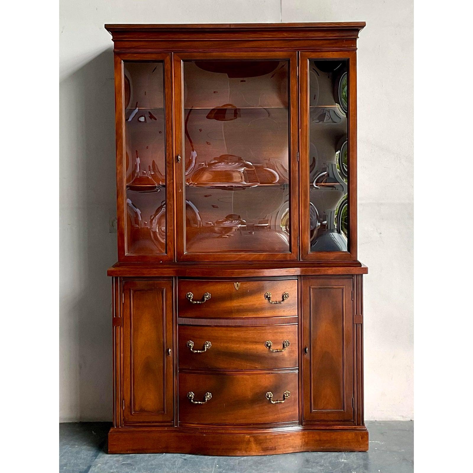 Ti presentiamo una sofisticata facciata vintage Hollywood Regency, un pezzo magnifico progettato per attirare l'attenzione ed elevare qualsiasi interno. Realizzata in ricco mogano, questa elegante vetrinetta è caratterizzata da un'elegante