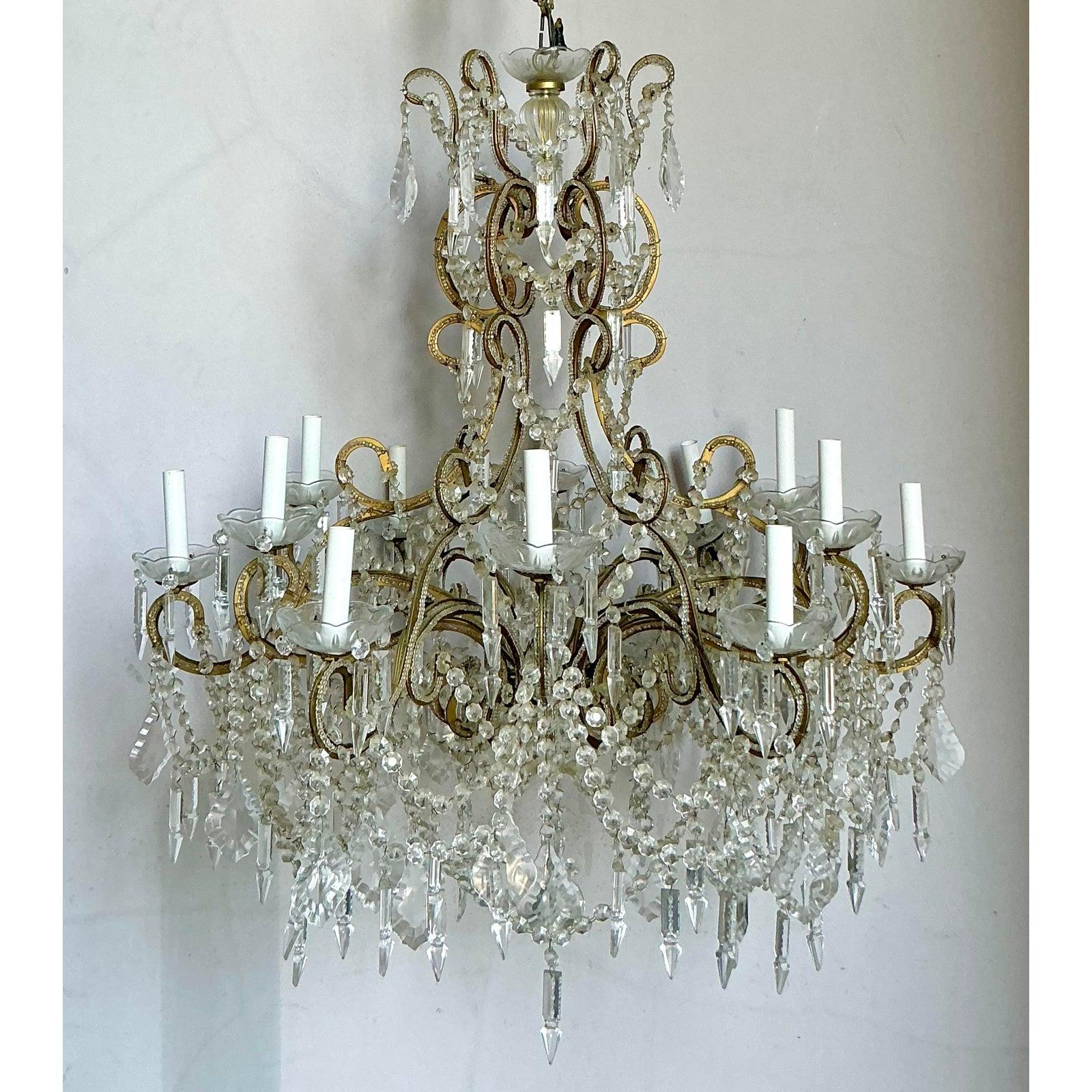 Questo spettacolare lampadario vintage cattura l'opulenza romantica del rococò e dello stile Hollywood Regency. Caratterizzata da una grande struttura a due livelli in ottone o metallo dorato, ornata da bracci a spirale e da un elaborato drappeggio