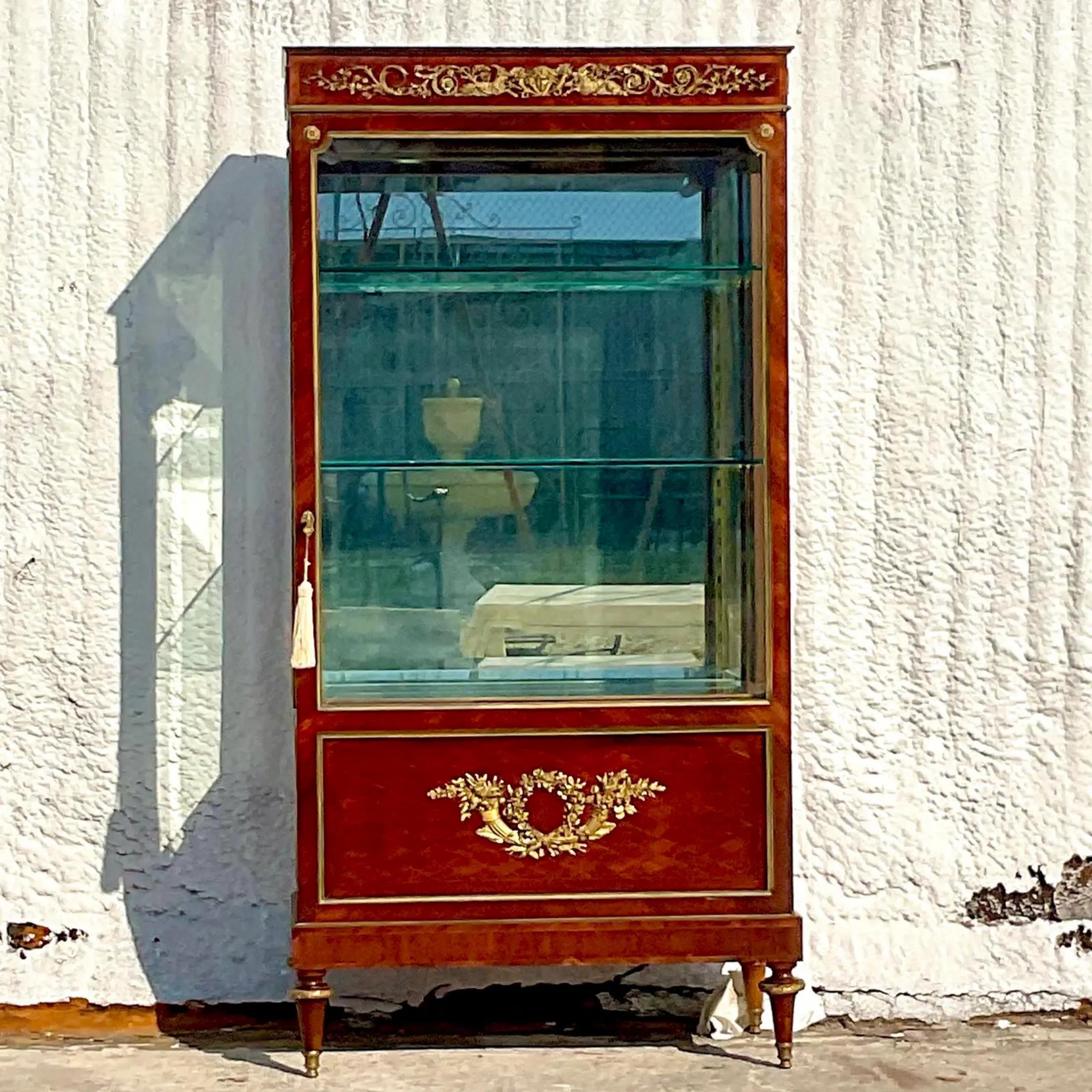 A fantastic vintage Empire glass cabinet. A chic mahogany with gorgeous Ormolu detail. Interior mirror and glass make the cabinet really light up. Acquired from a Palm Beach estate