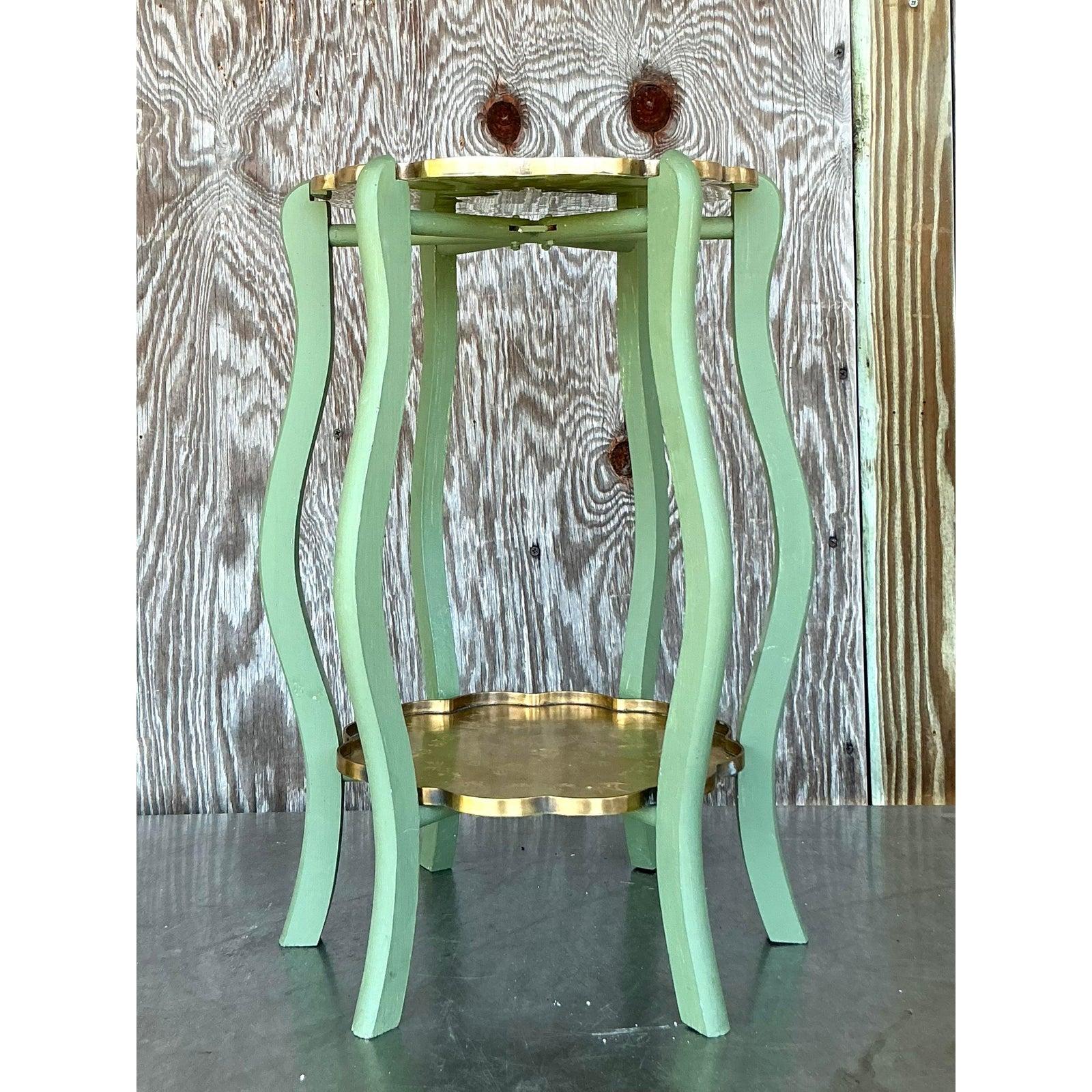 Ajoutez une touche de sophistication vintage à votre espace avec cette charmante table d'appoint à deux niveaux de style Regency. Avec ses plateaux en laiton gravé dans une teinte dorée et ses pieds en bois vert élégamment incurvés, cette petite