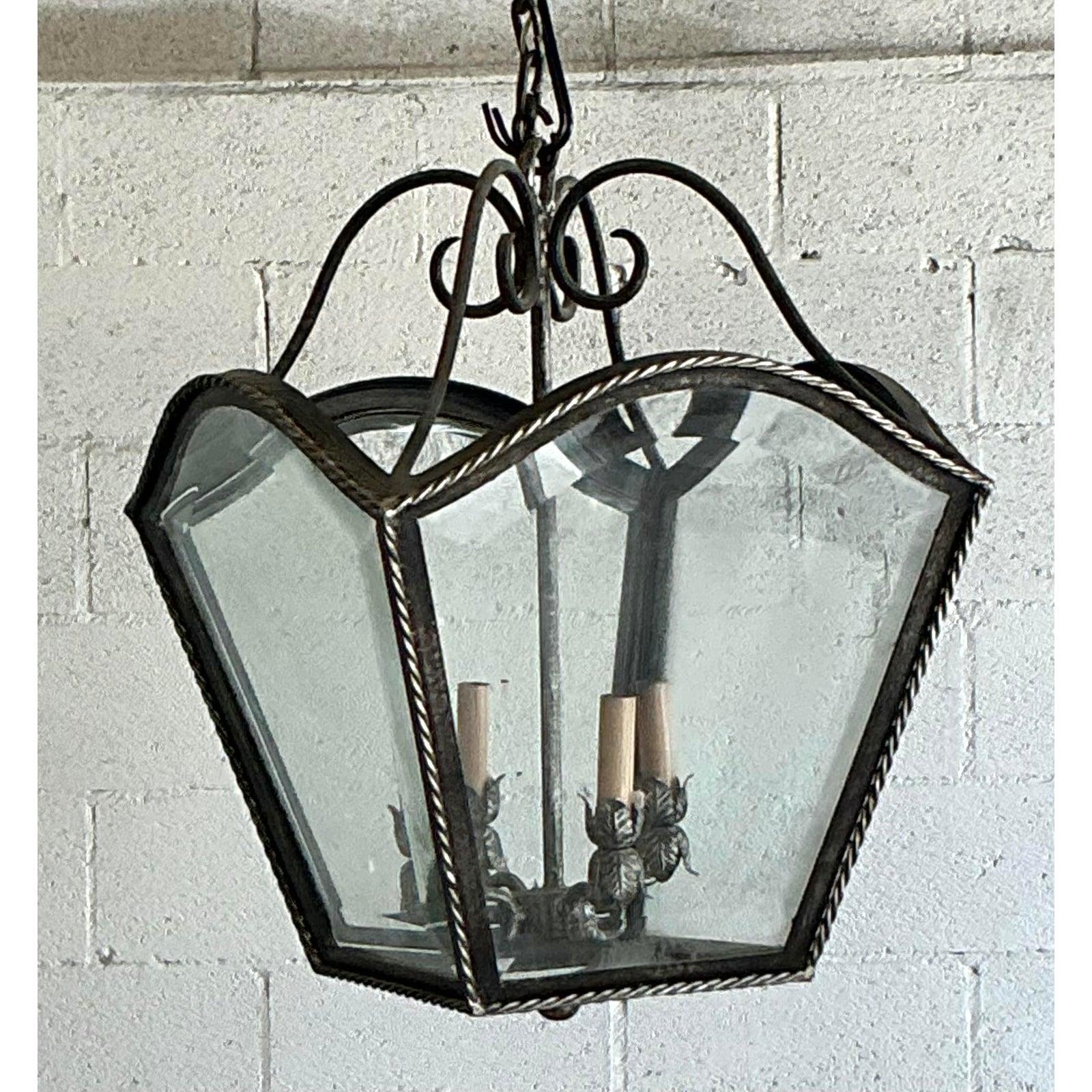 Introduce a touch of classic sophistication to your home with this stunning vintage French Regency style lantern. Masterfully crafted, its graceful silhouette features four curved glass panels encased in a dark wrought iron frame, creating an