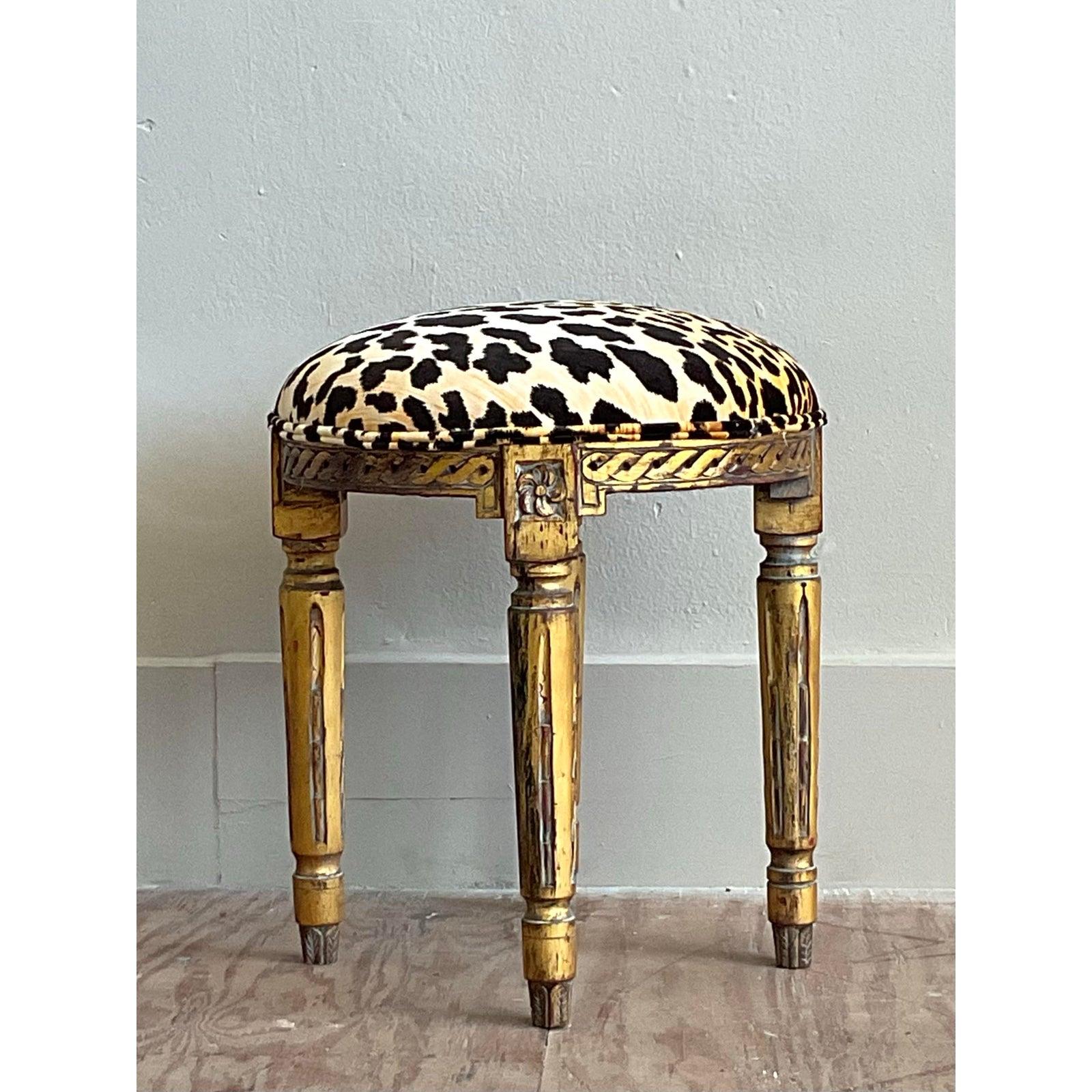 Exhalant un air de drame sophistiqué, ce tabouret vintage est un mélange magistral d'élégance Regency et de glamour hollywoodien. Le cadre rond classique se distingue par sa riche finition en bois doré antique et ses détails sculptés, notamment un
