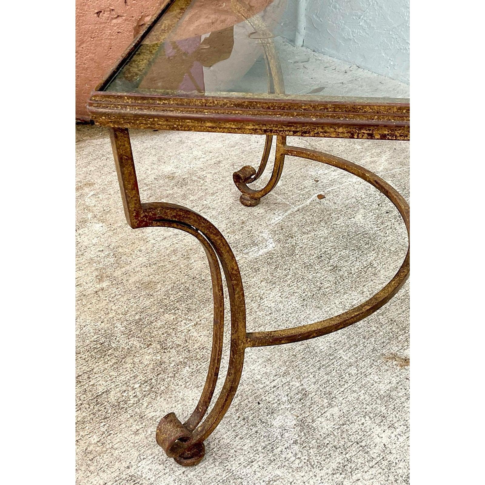 Infuse your living space with timeless European elegance with this beautifully crafted vintage coffee table. The piece features a gracefully designed gilt iron base, showcasing delicate, scrolling legs and a central stretcher that speak to its