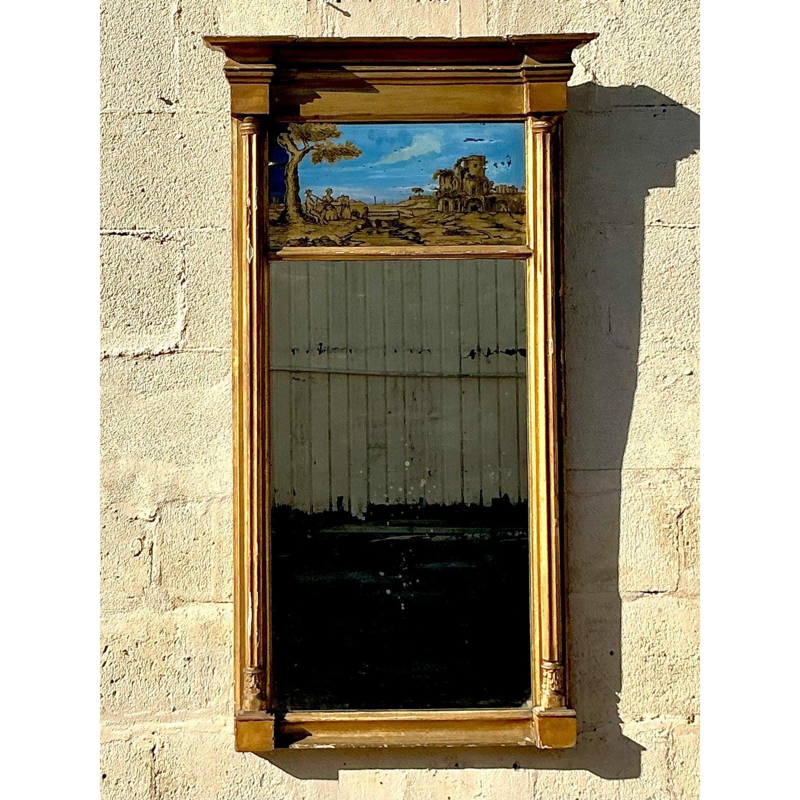 Rehaussez votre décor avec cet exquis miroir Vintage Regency Gilt Eglomise, une pièce intemporelle qui respire l'élégance et le charme historique. Ce miroir est encadré d'une bordure en bois doré avec des détails néoclassiques, reflétant l'opulence