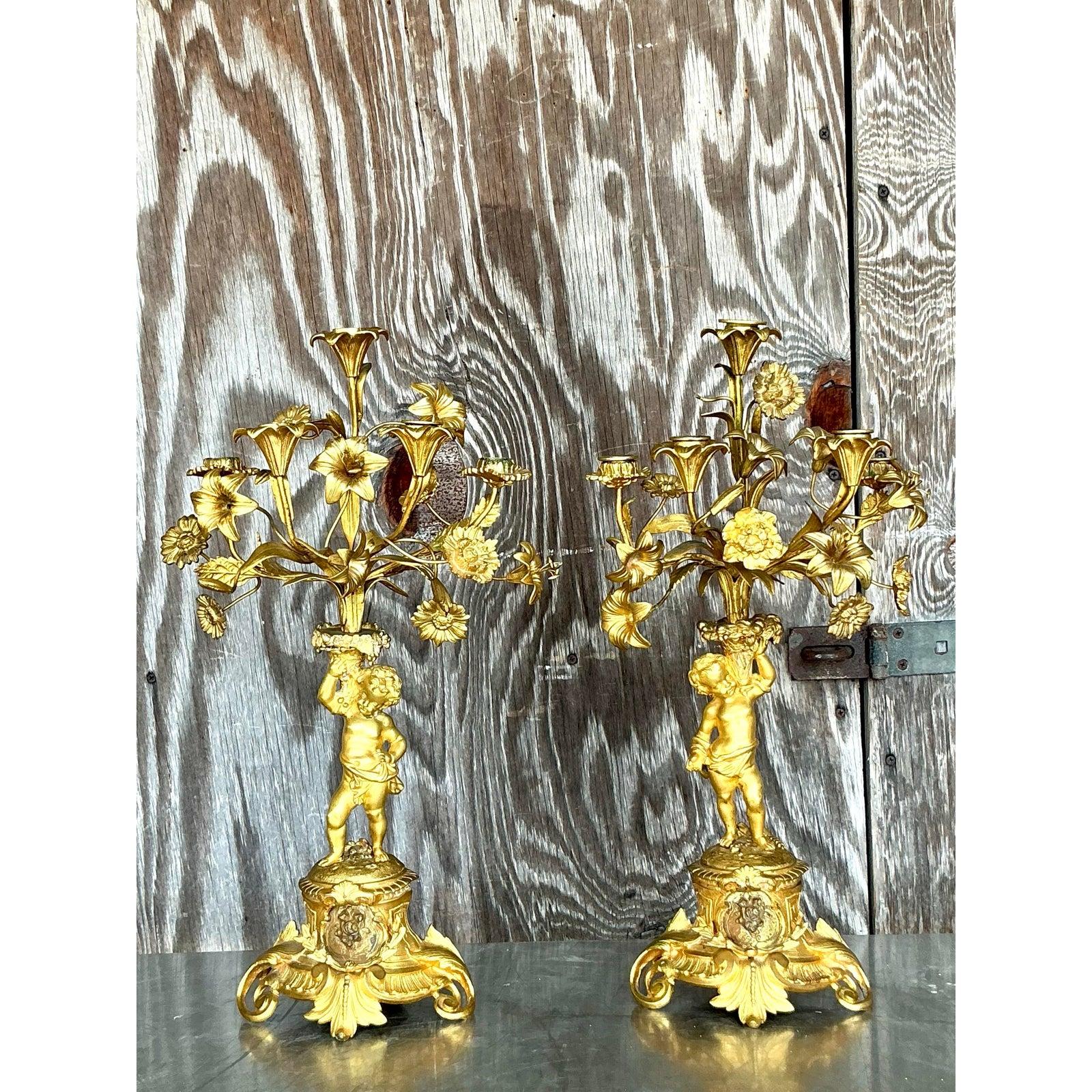 Discover the opulent charm of these Vintage Regency Gilt Floral Cherub Candelabras, a stunning pair from the 1950s that exudes French elegance. Crafted from gilt brass, each candelabra features a cherub holding a bouquet of intricately detailed