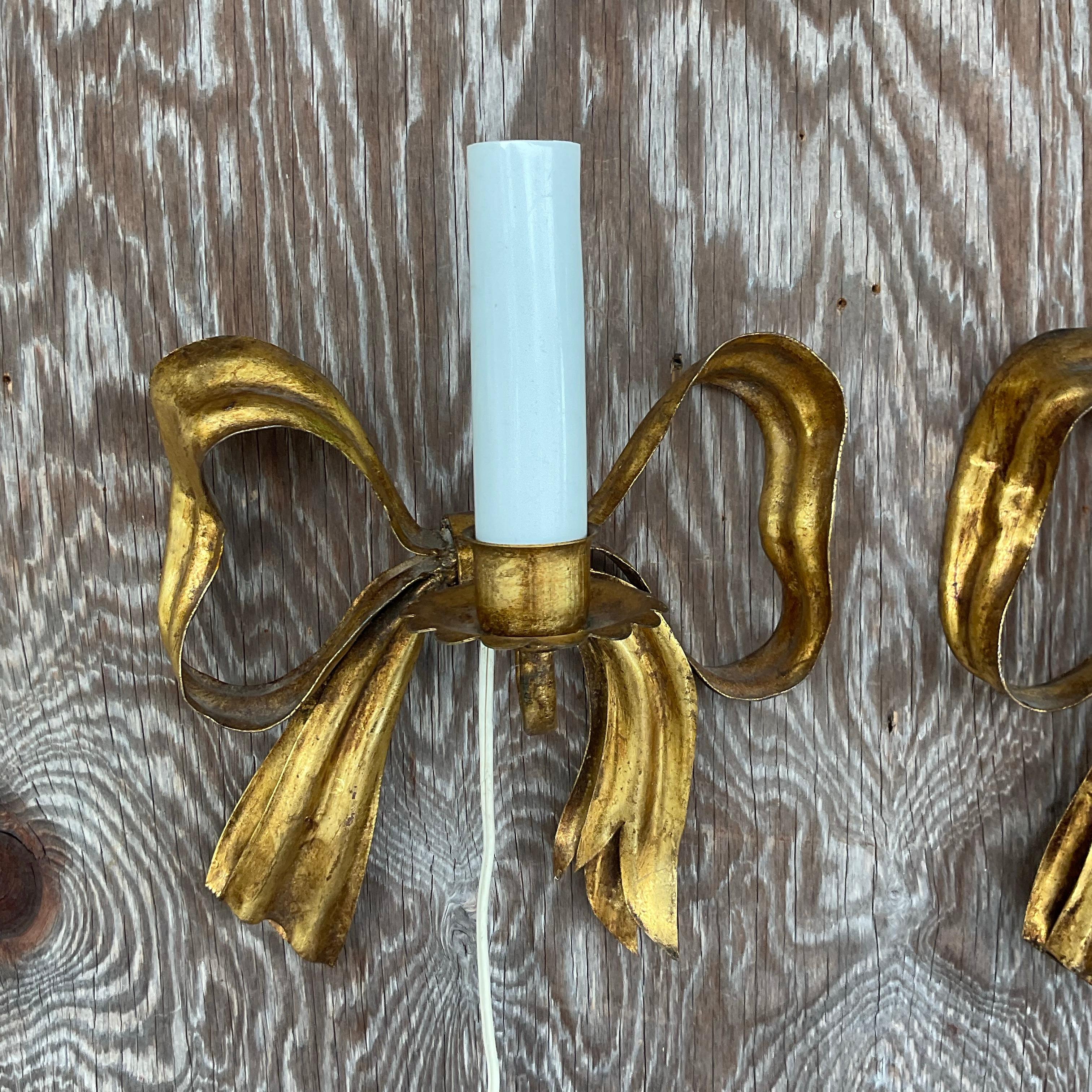 Elevate your décor with a touch of timeless elegance courtesy of our Vintage Regency Gilt Metal Bow Sconces - A Pair. Crafted with meticulous attention to detail, these American-made treasures exude sophistication and add a regal flair to any space