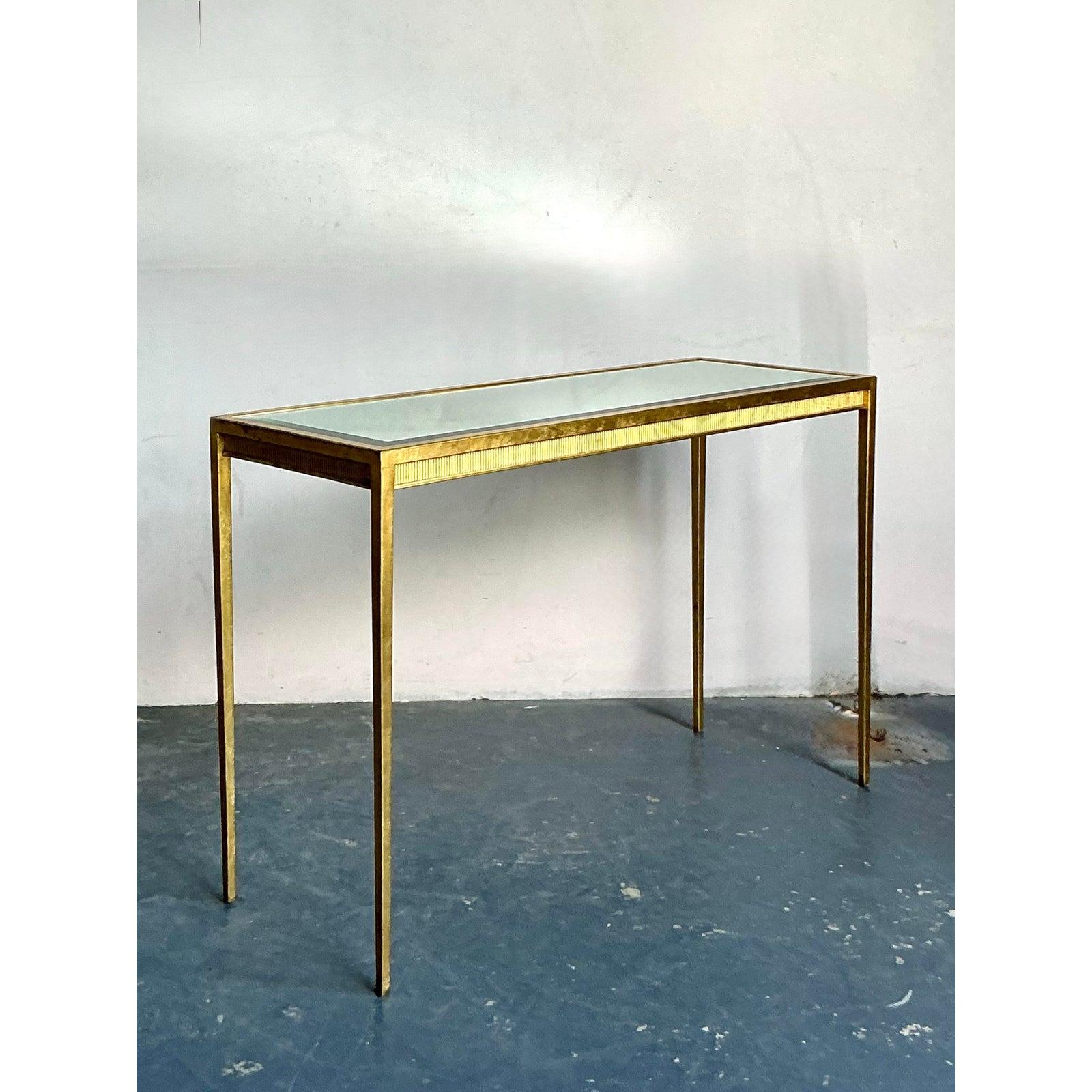 This elegant vintage console table is a quintessential piece of Hollywood Regency glamour, defined by its clean lines and rich, golden finish. The table features a sleek, minimalist frame crafted from gilt metal, which has a beautiful aged patina