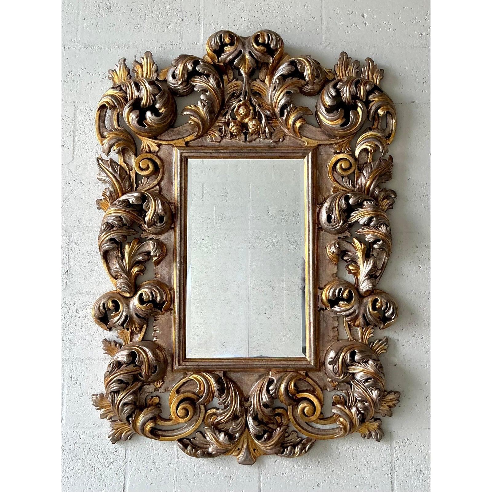 Introduci un tocco mozzafiato di opulenza d'altri tempi con questo magnifico specchio a volute vintage. La cornice profondamente intagliata è una masterclass di arte barocca, con un'esplosione di foglie d'acanto scultoree e drammatiche volute a C