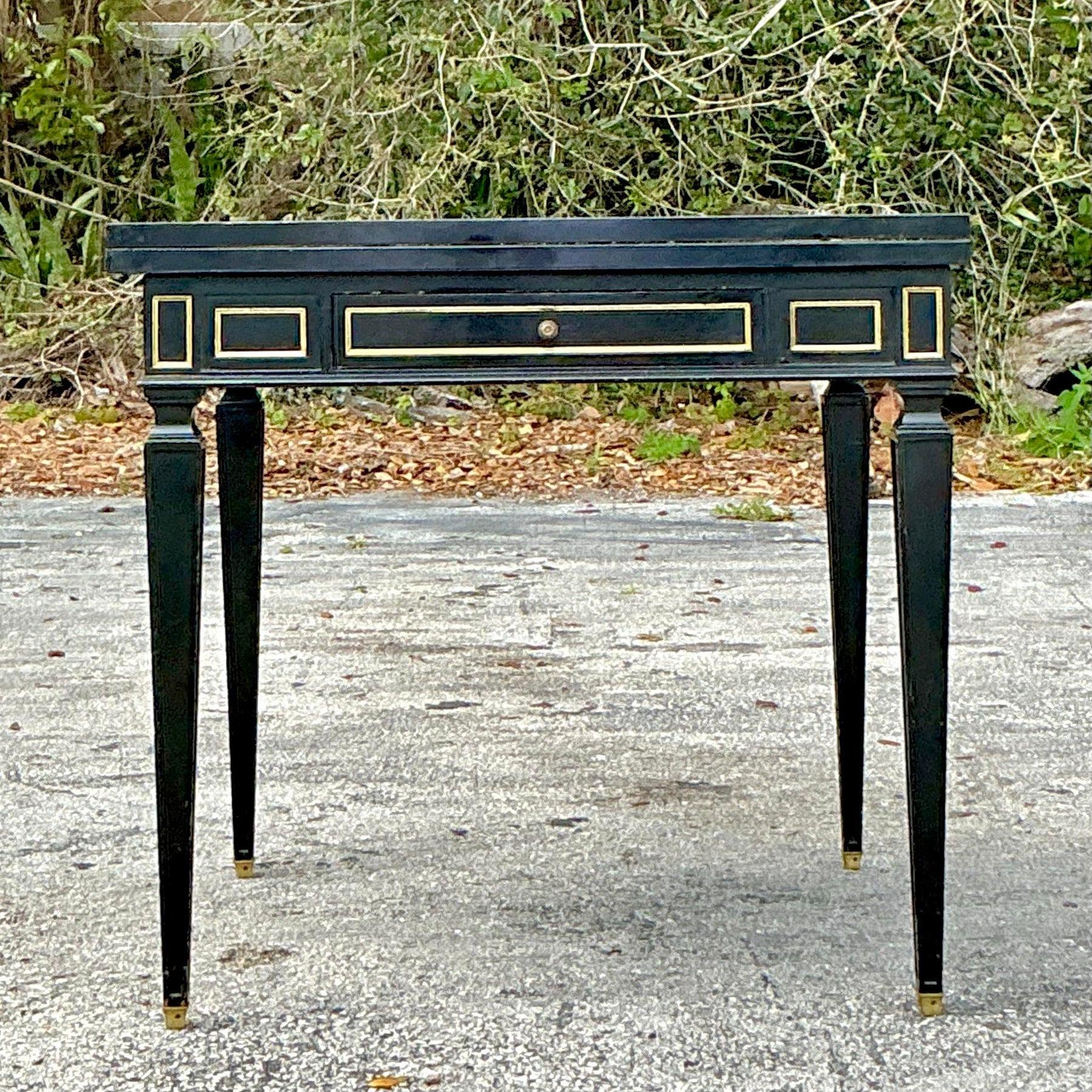 This exquisite vintage Regency flip-top game table combines elegance with versatility. Featuring a sleek black lacquer finish with refined gilt accents, this piece boasts a sophisticated aesthetic. The tapered legs, brass-capped feet, and gold