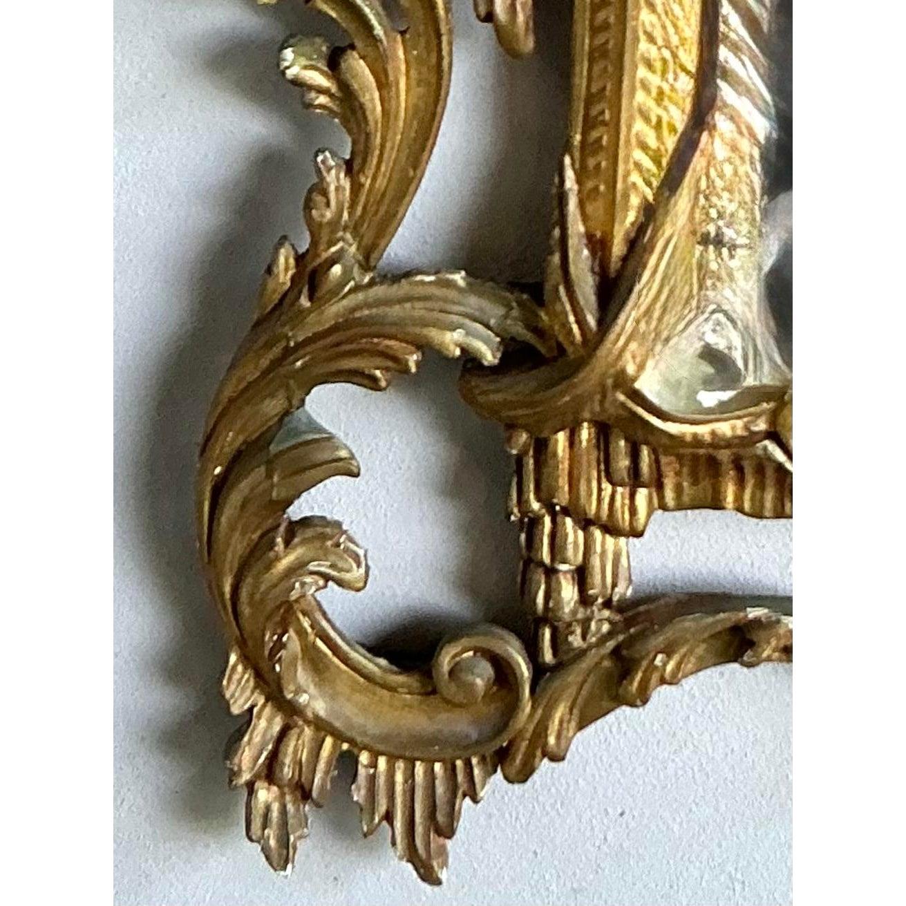 Questo spettacolare specchio è una testimonianza del drammatico design Hollywood Regency, che trae ispirazione dagli opulenti motivi rococò del XVIII secolo e aggiunge un tocco esotico con il suo stemma in stile pagoda. La cornice pesantemente