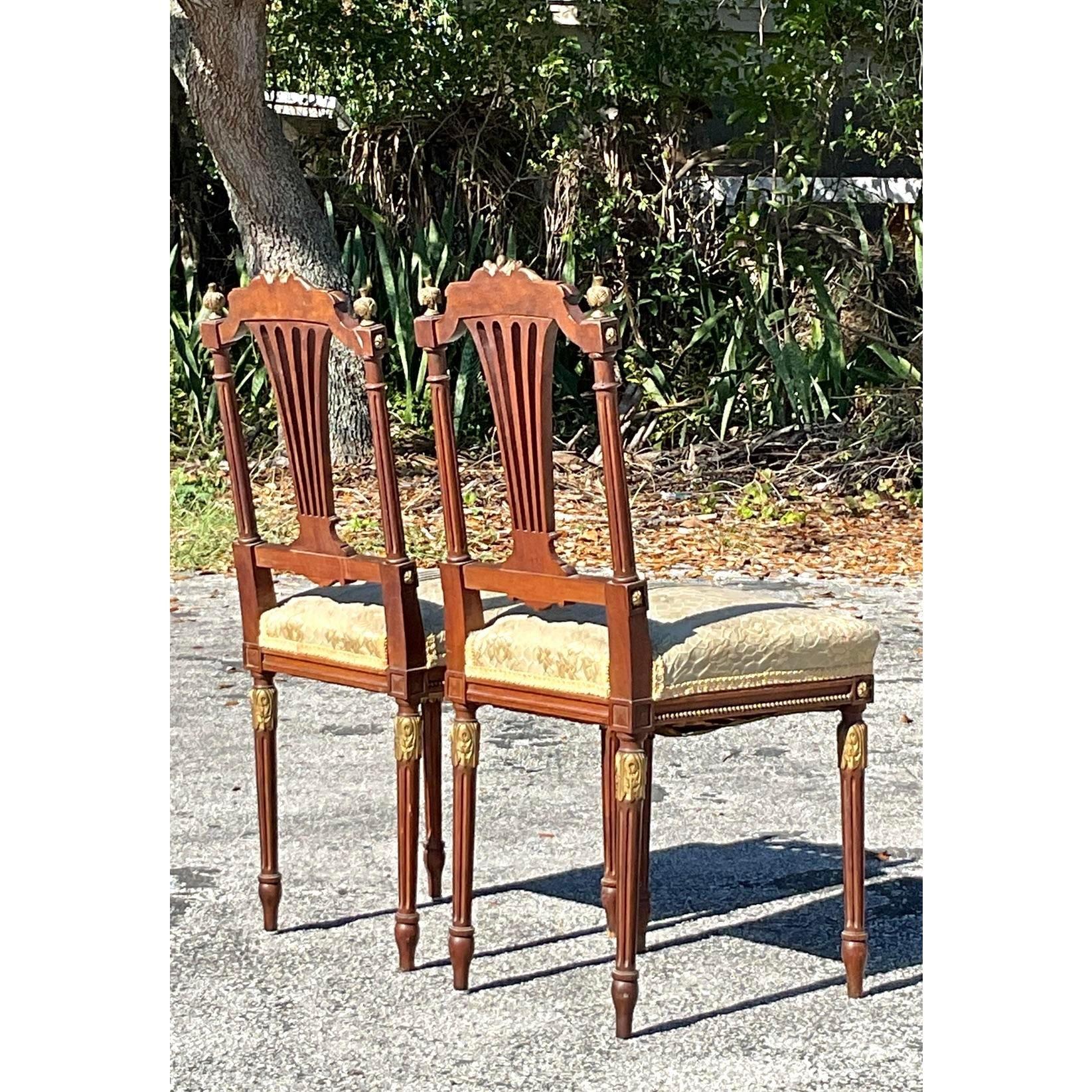 Elégamment conçue grâce à un travail artisanal complexe, cette paire de chaises d'appoint vintage de style Regency présente des accents dorés exquis et des cadres en bois finement sculptés. Le délicat design du dossier à cannelures, orné de détails