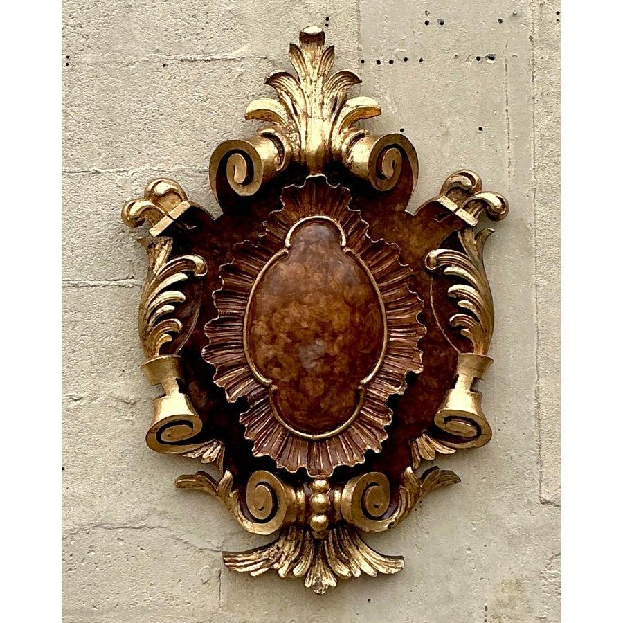 Rehaussez votre intérieur avec cet exquis cartouche en bois doré de style Regency. Conçu de façon magistrale avec des détails de volutes opulentes et une riche finition dorée, cet accent décoratif exsude une élégance et un charme intemporels. Le