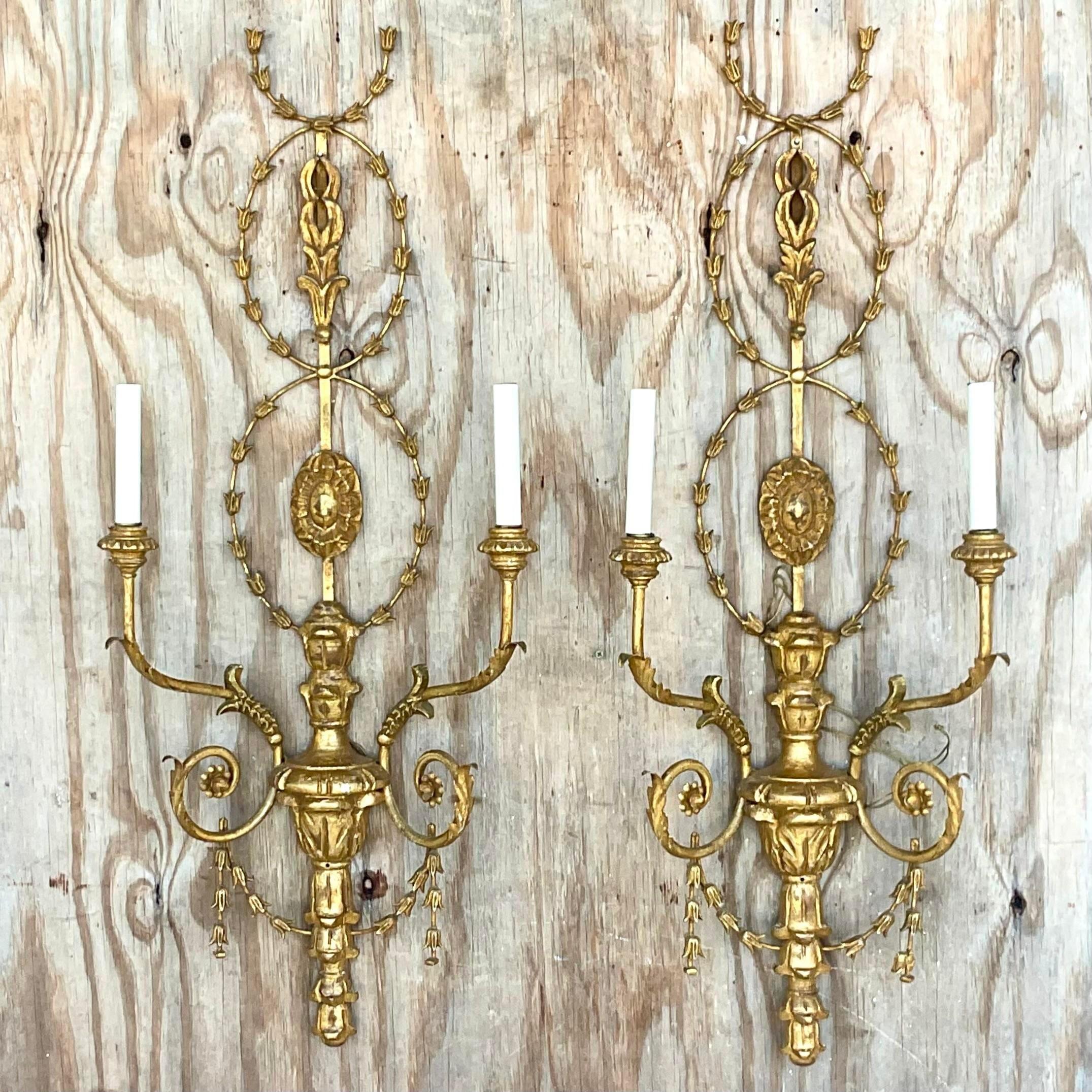 A fantastic pair of vintage Regency wall sconces. Chic gesso over carved wood in a wrapping garland design. Bright gilt finish. Acquired from a Palm Beach estate.