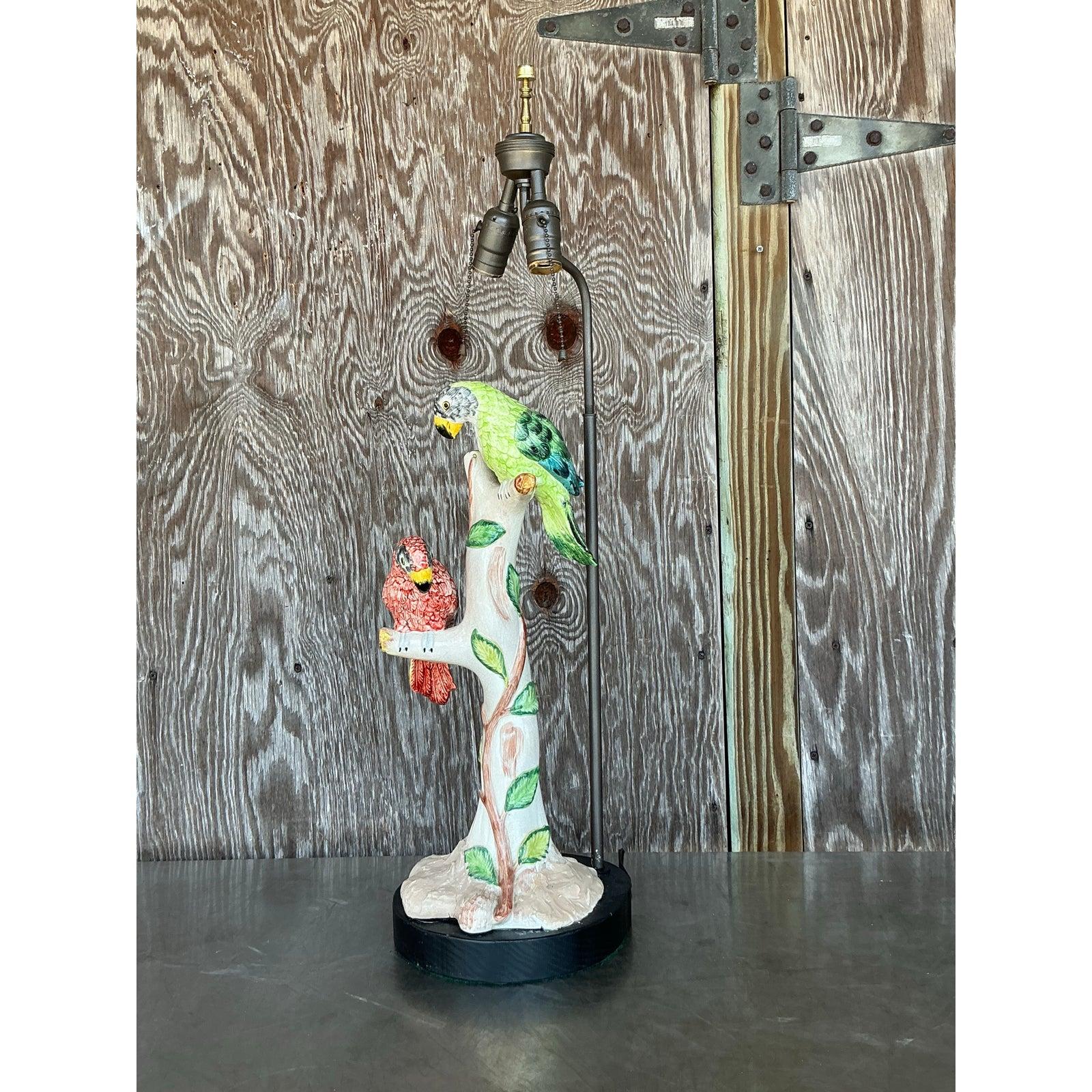 Ajoutez une touche vibrante de caractère à votre espace avec cette charmante lampe oiseau vintage en céramique de style Régence. Perchés sur une base sculpturale en forme d'arbre, deux perroquets - l'un d'un rouge éclatant, l'autre d'un vert