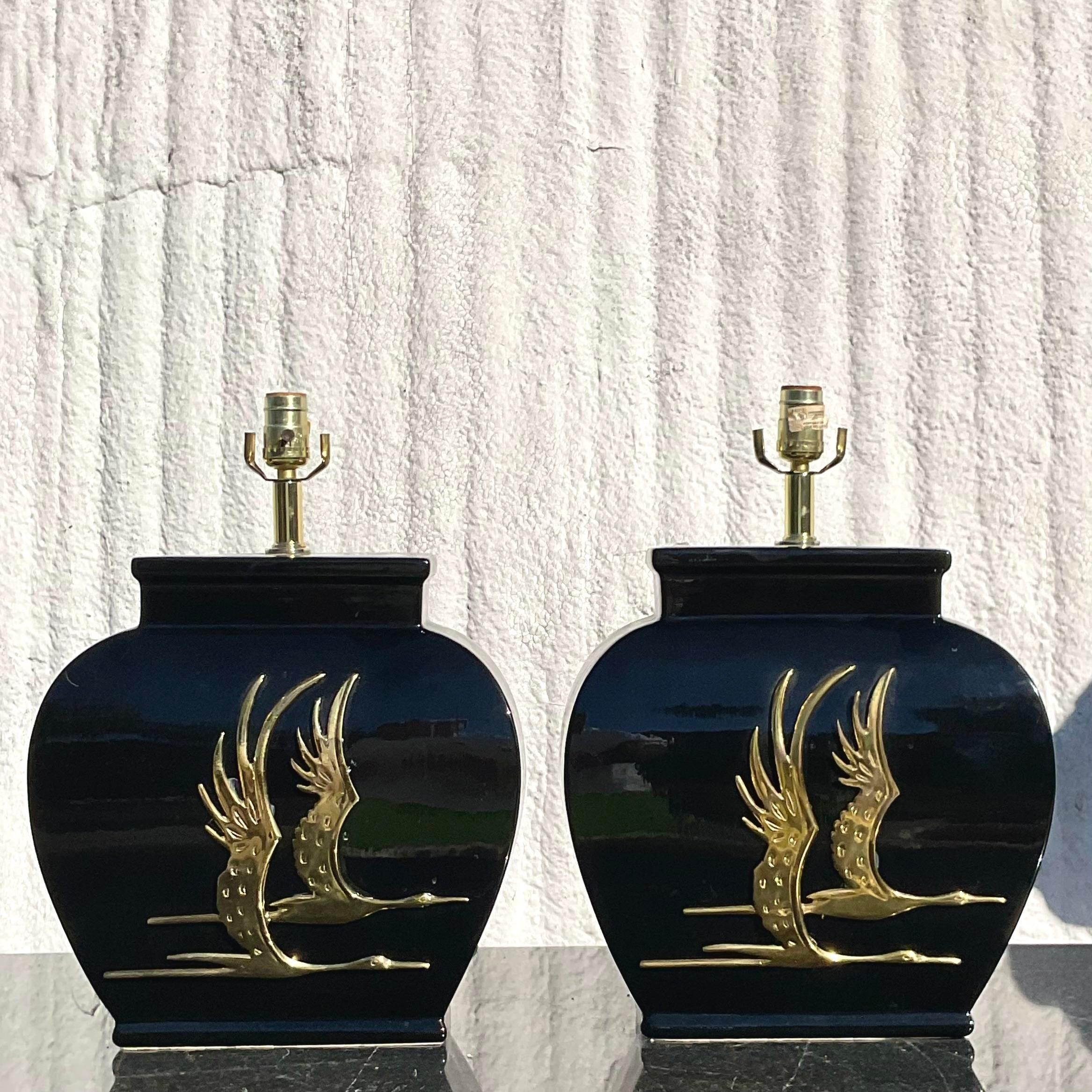 A fantastic pair of vintage Regency table lamps. A chic black glazed ceramic with brass herons flying across the front. Acquired from a Palm Beach estate.