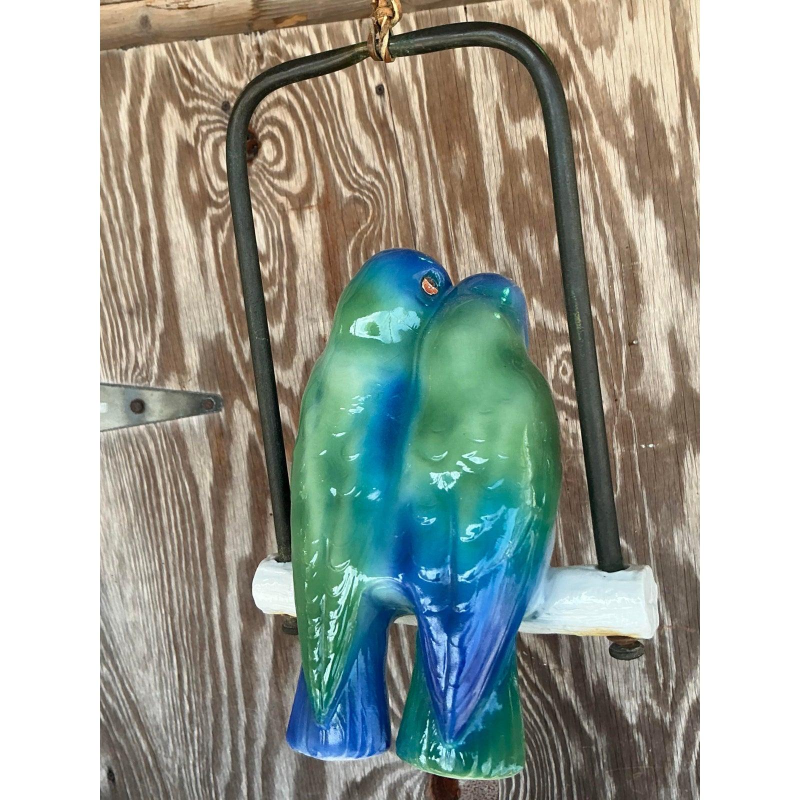 Aggiungi un tocco di romanticismo e charme al tuo spazio con questa scultura in ceramica smaltata Vintage Regency Lovebirds. Appollaiati su un trespolo in ceramica e racchiusi in un'altalena minimale in metallo nero, questi uccellini resi in modo