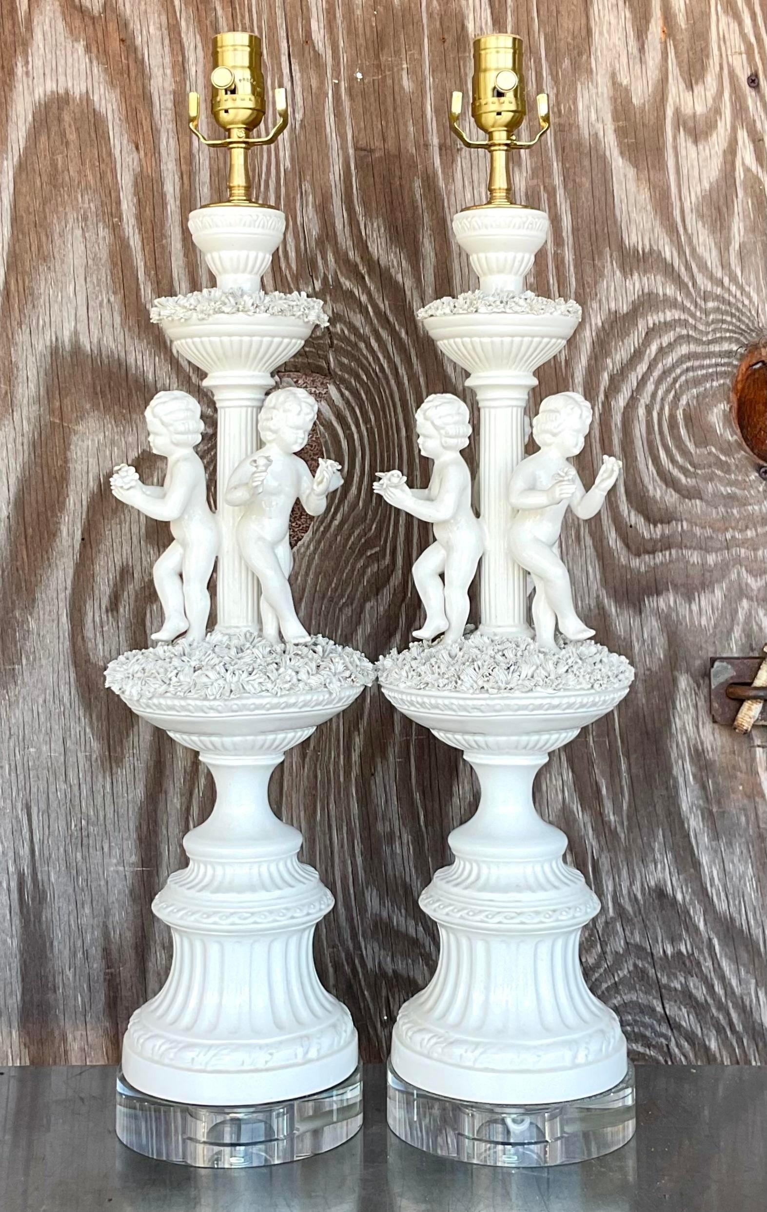 A fabulous pair of vintage Regency table lamps. Done in the manner of thr Putti style cherubs. A chic glazed ceramic finish with a bright white color. Fully restored with all new Wiring, hardware and lucite plinths. Acquired from a Palm Beach estate.
