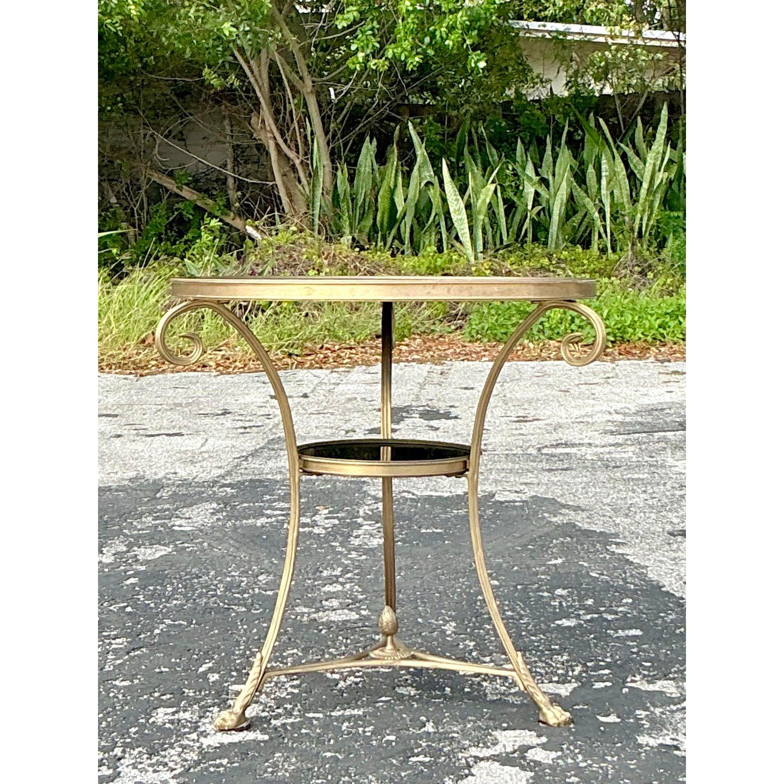 Add a touch of classic elegance to your space with this Vintage Regency Global Views Directoire Gueridon Table. Featuring a graceful curved gilt metal frame, this refined accent table showcases a round black glass top and matching lower tier,
