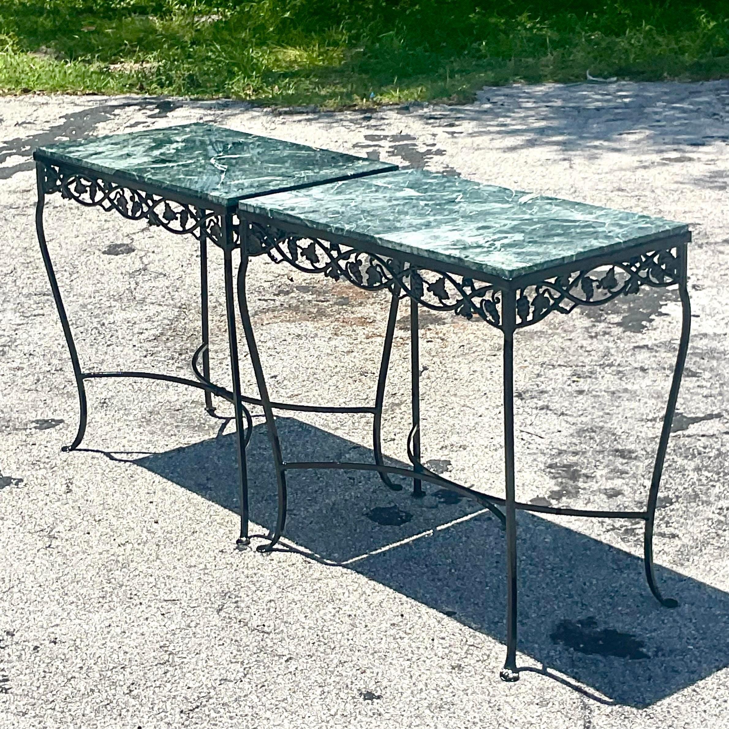 A stunning pair of vintage Regency outdoor console tables. Beautiful floral wrought iron with inset green marble tops. Recently powder-coated in gloss black. Acquired from a Palm Beach estate.