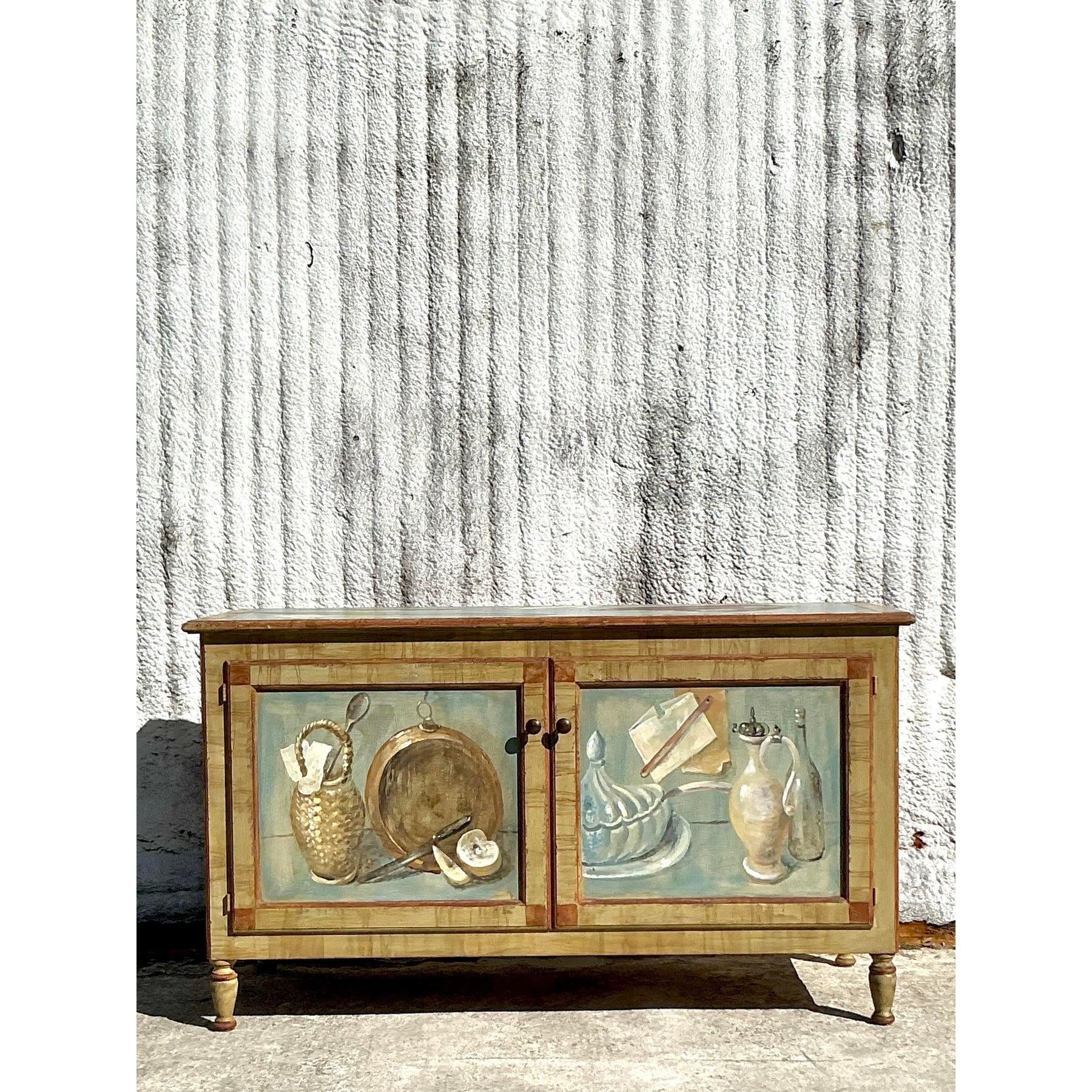This elegant vintage Regency hand-painted cabinet is a masterpiece of functional art, featuring delicately painted panels with charming still-life motifs. The rich detailing and soft, muted hues create a timeless appeal that complements a variety of