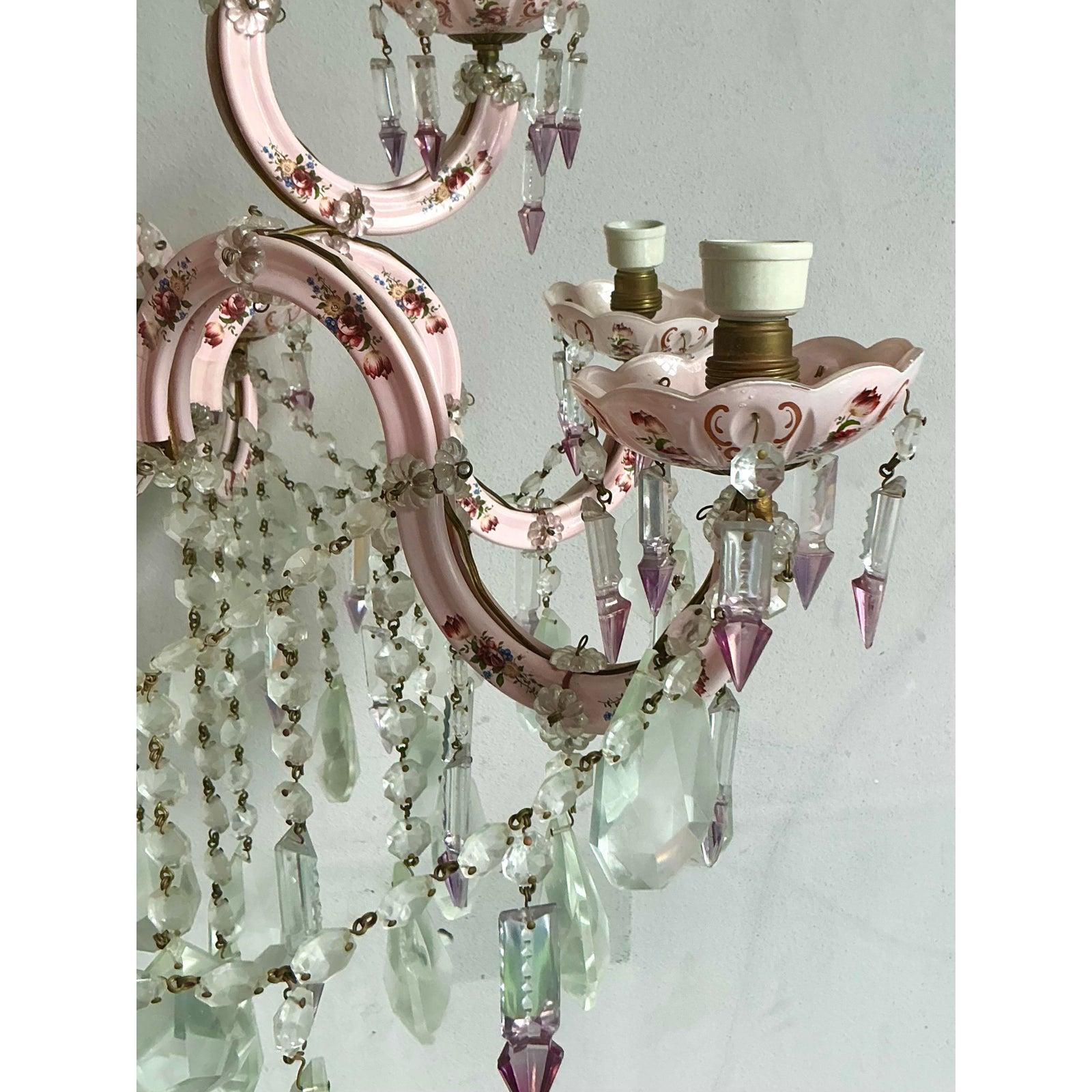Faites une déclaration à couper le souffle avec ce lustre vintage exquis de style Regency. Véritable chef-d'œuvre de design romantique, ce luminaire se compose d'un cadre métallique gracieusement étagé, fini dans un délicat rose tendre et orné de