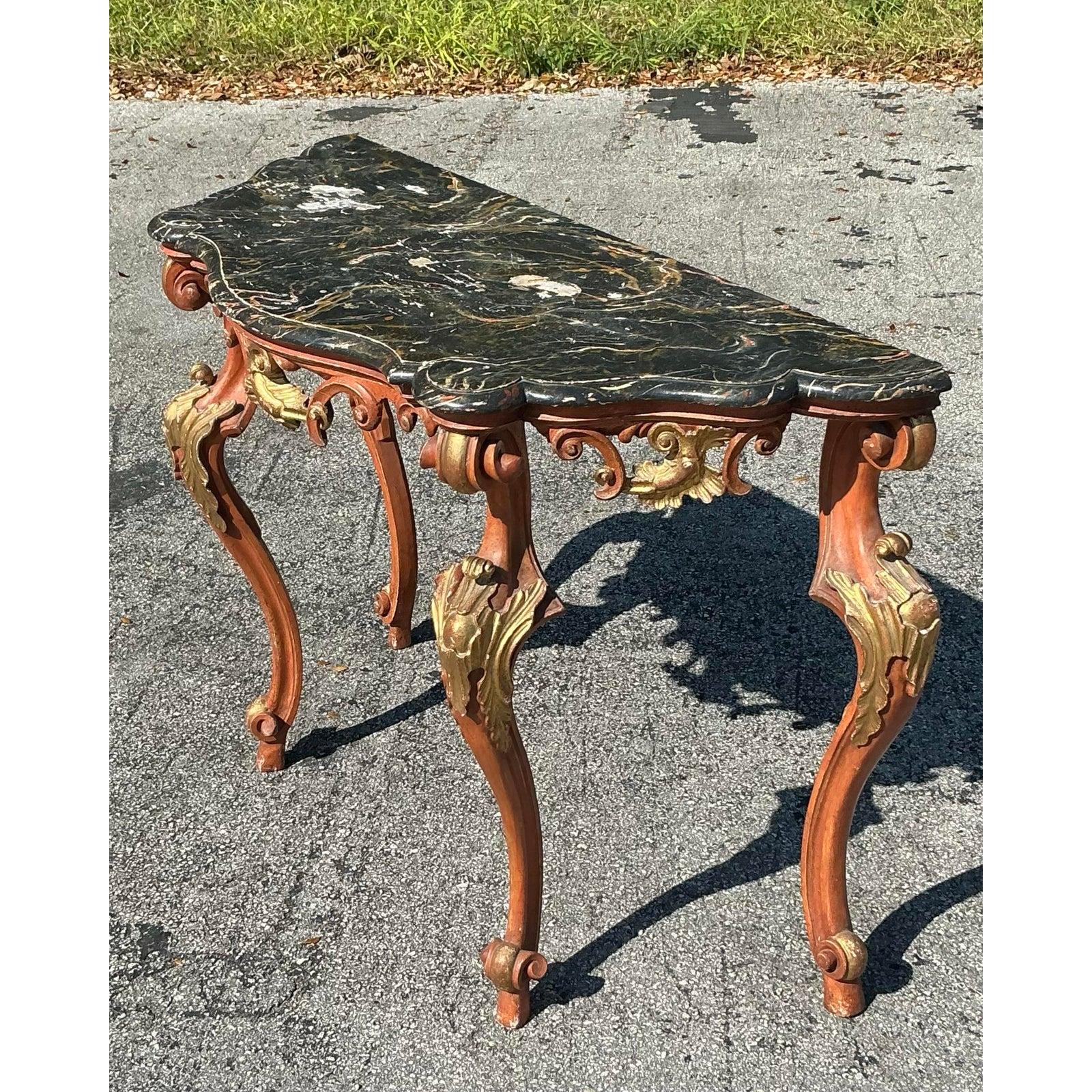 Cette exquise table console vintage Regency Rococo incarne l'élégance européenne d'antan avec son cadre en bois sculpté peint à la main et son superbe plateau en marbre noir. Les pieds cabriole joliment incurvés sont ornés de sculptures décoratives