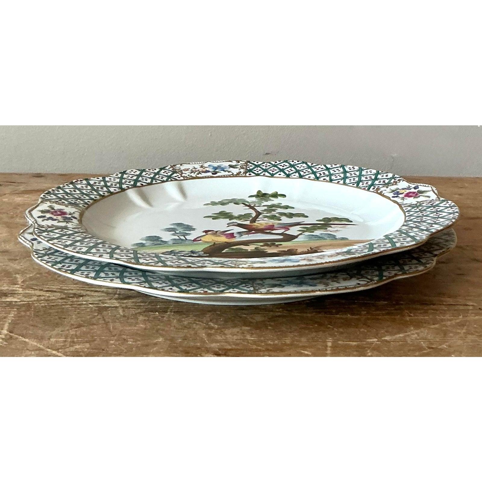 This beautiful pair of porcelain dinner plates showcases a delightful blend of traditional European form and exotic Chinoiserie decoration. Each plate features an appealing scalloped edge finished with fine gold gilt, framing a broad border adorned