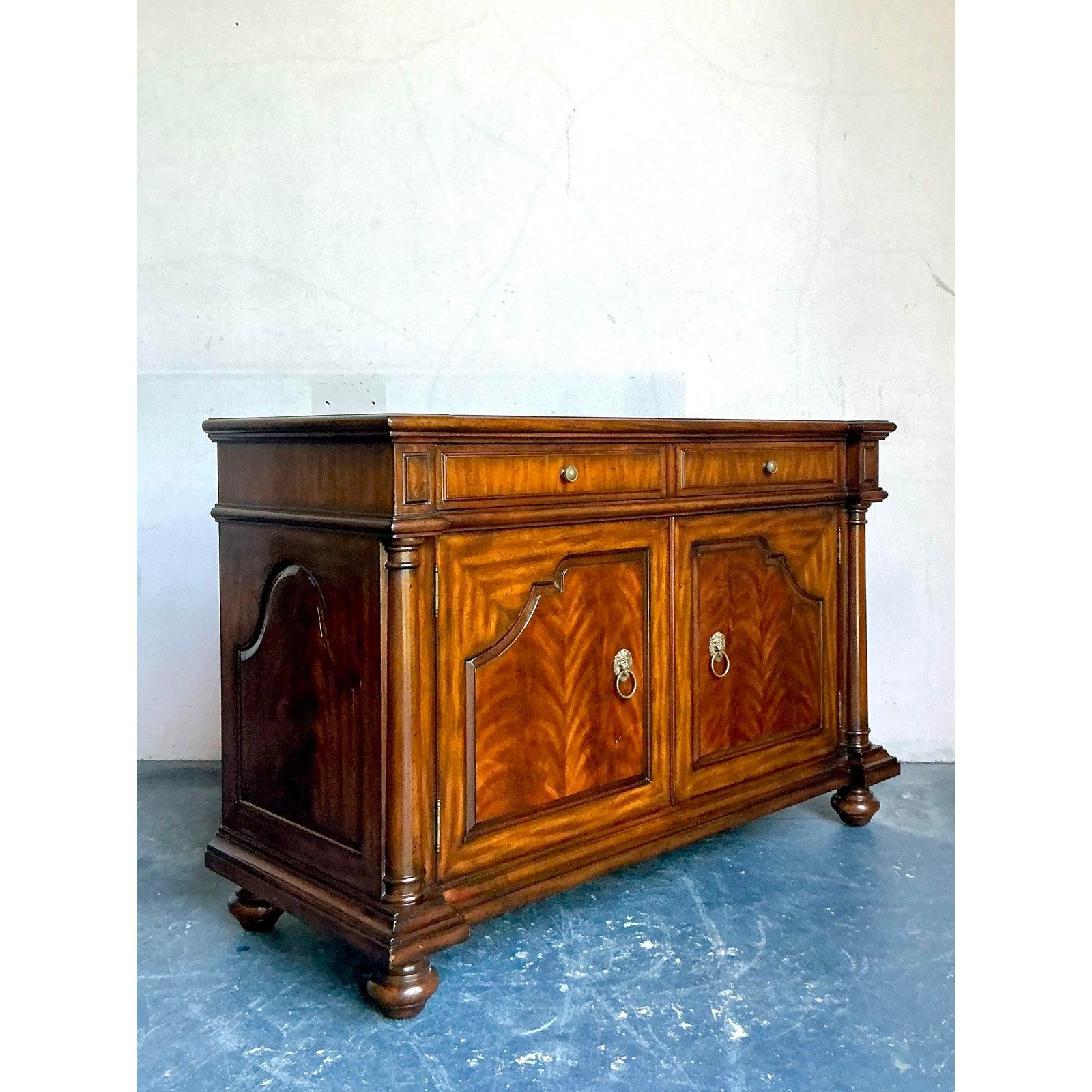 This exceptional sideboard, produced by the renowned Maitland-Smith company, is a stunning revival of Neoclassical and English Regency design. Crafted from rich mahogany, the cabinet features striking figured veneer panels and elegant bun feet,