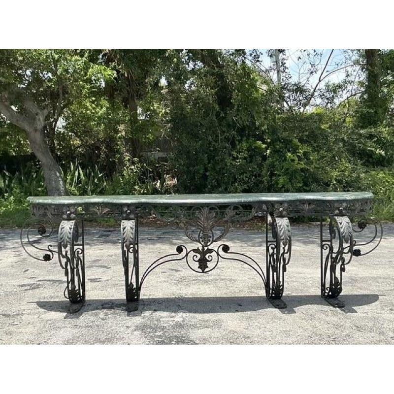 Command attention and define your space with this truly monumental vintage Regency-style console table. Its expansive, richly veined green marble top, boasting a gracefully serpentine edge, rests upon an incredibly ornate and robust wrought iron
