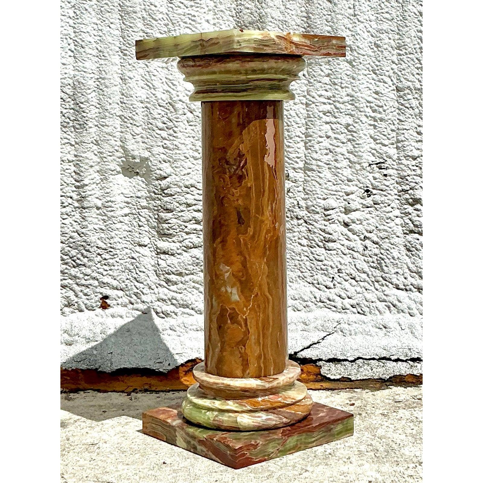 Élevez votre espace avec ce piédestal Vintage Regency Onyx exquis, une fusion frappante de la forme classique et de l'art de la pierre naturelle. Fabriqué en onyx richement veiné, ce piédestal en forme de colonne présente une palette captivante de