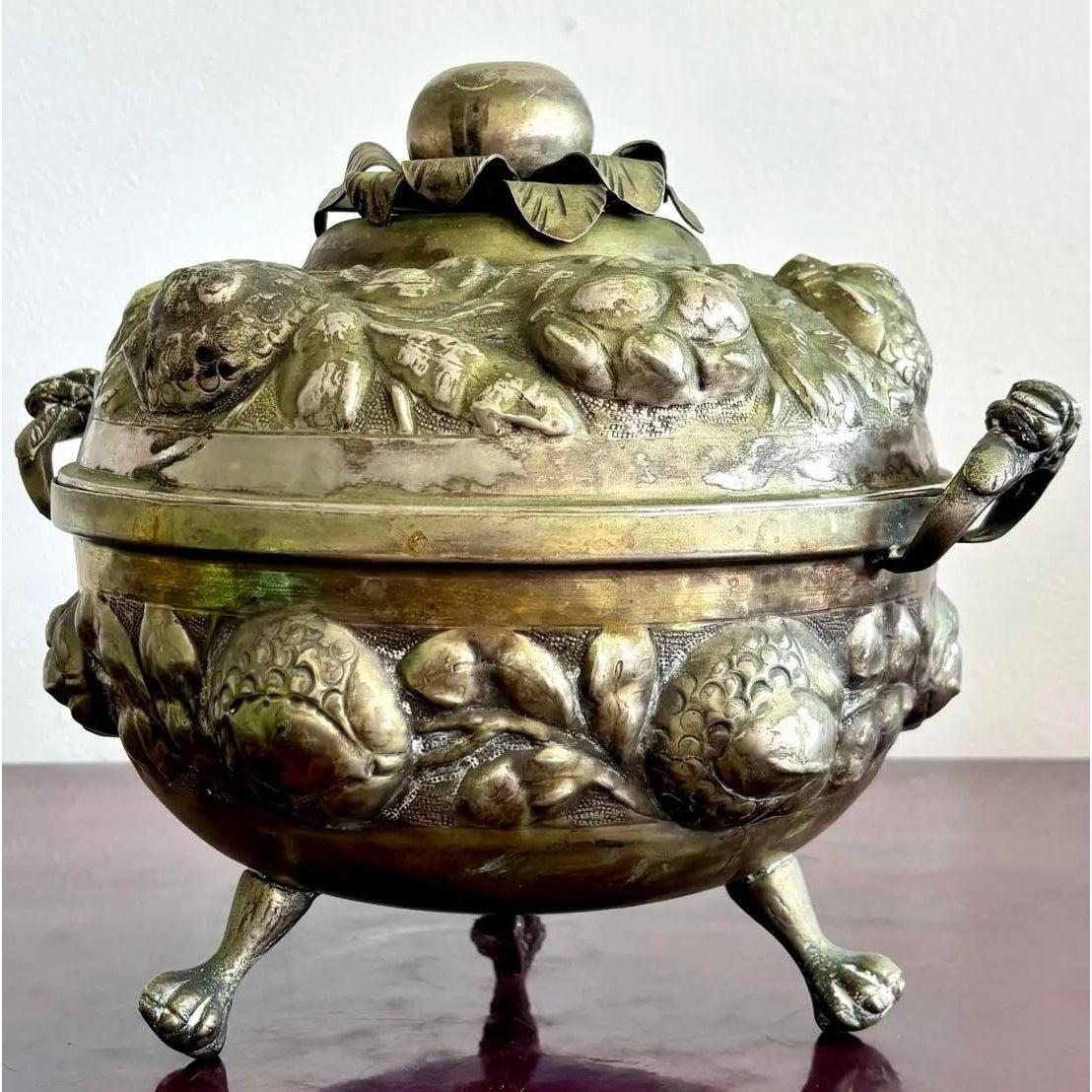 Este ornamentado recipiente de plata irradia la grandeza del Viejo Mundo, con su superficie ricamente repujada repleta de frutas, hojas y diminutos crustáceos, casi como una cosecha desbordante. La tapa abovedada está coronada por un remate