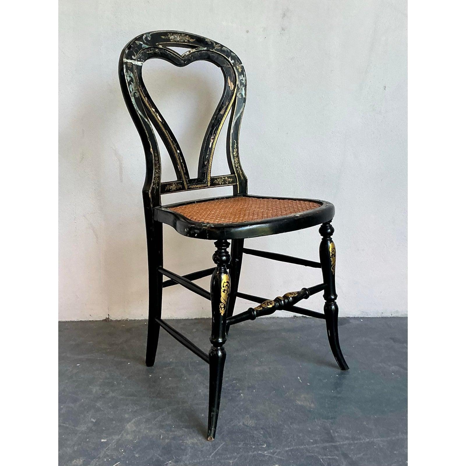 Brimming with Victorian-era charm, this exquisite side chair is a remarkable work of art. The frame is crafted from ebonized wood or papier-mâché, featuring a romantic heart-shaped back and gracefully turned legs. Its deep, black lacquered surface