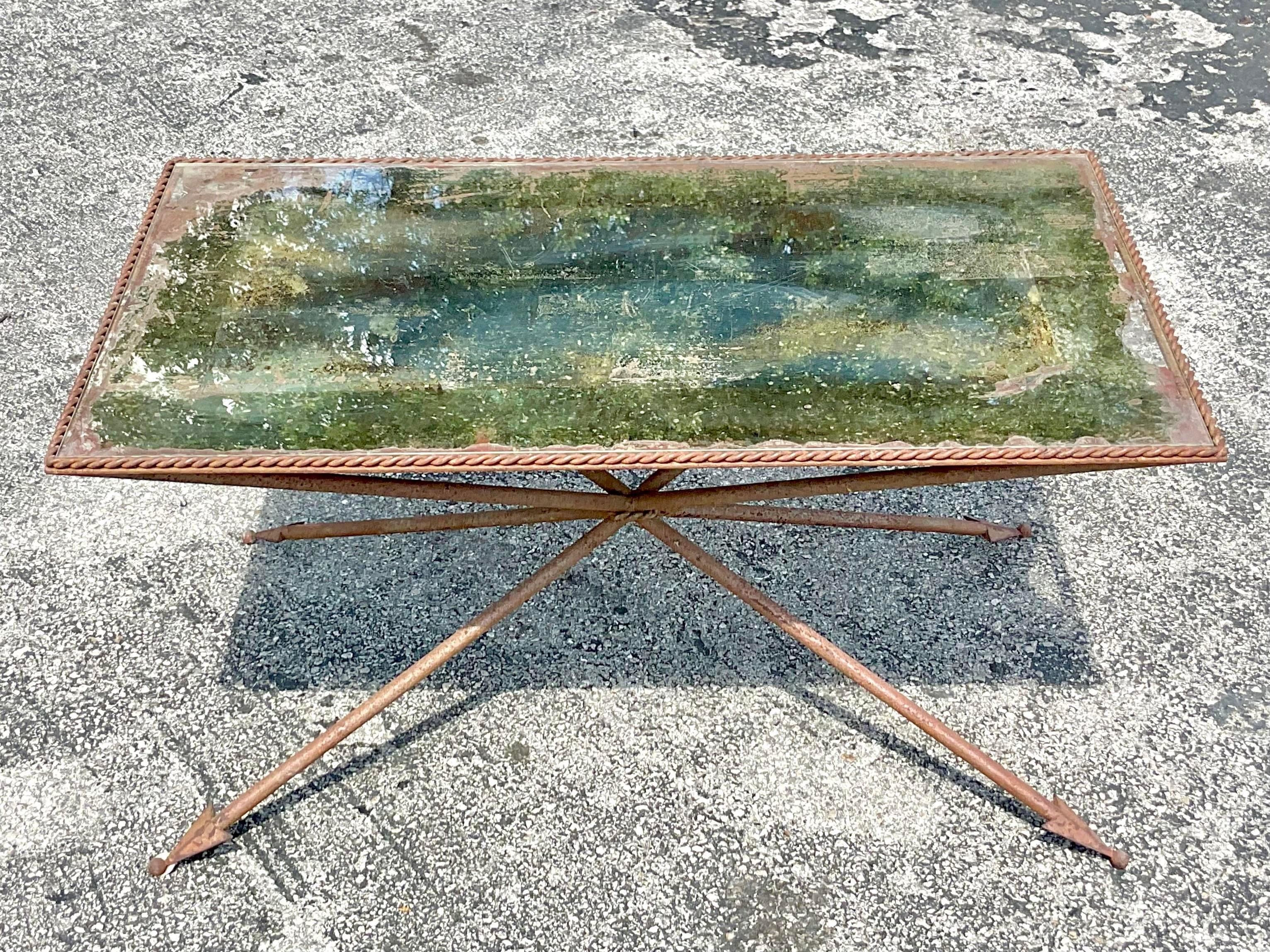 An exceptional vintage Regency coffee table. A brilliant Directorie style table with an all over patinated finish. Beautiful distressed inset mirrored top and arrow legs. Acquired from a Palm Beach estate.