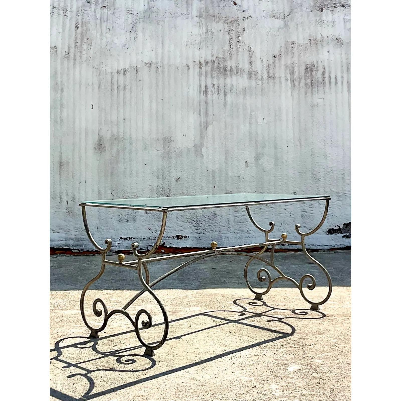Fantastic vintage Regency console table. A chic scroll design with a silver patinated finish. A glass top rests on the frame. Acquired from a Palm Beach estate.