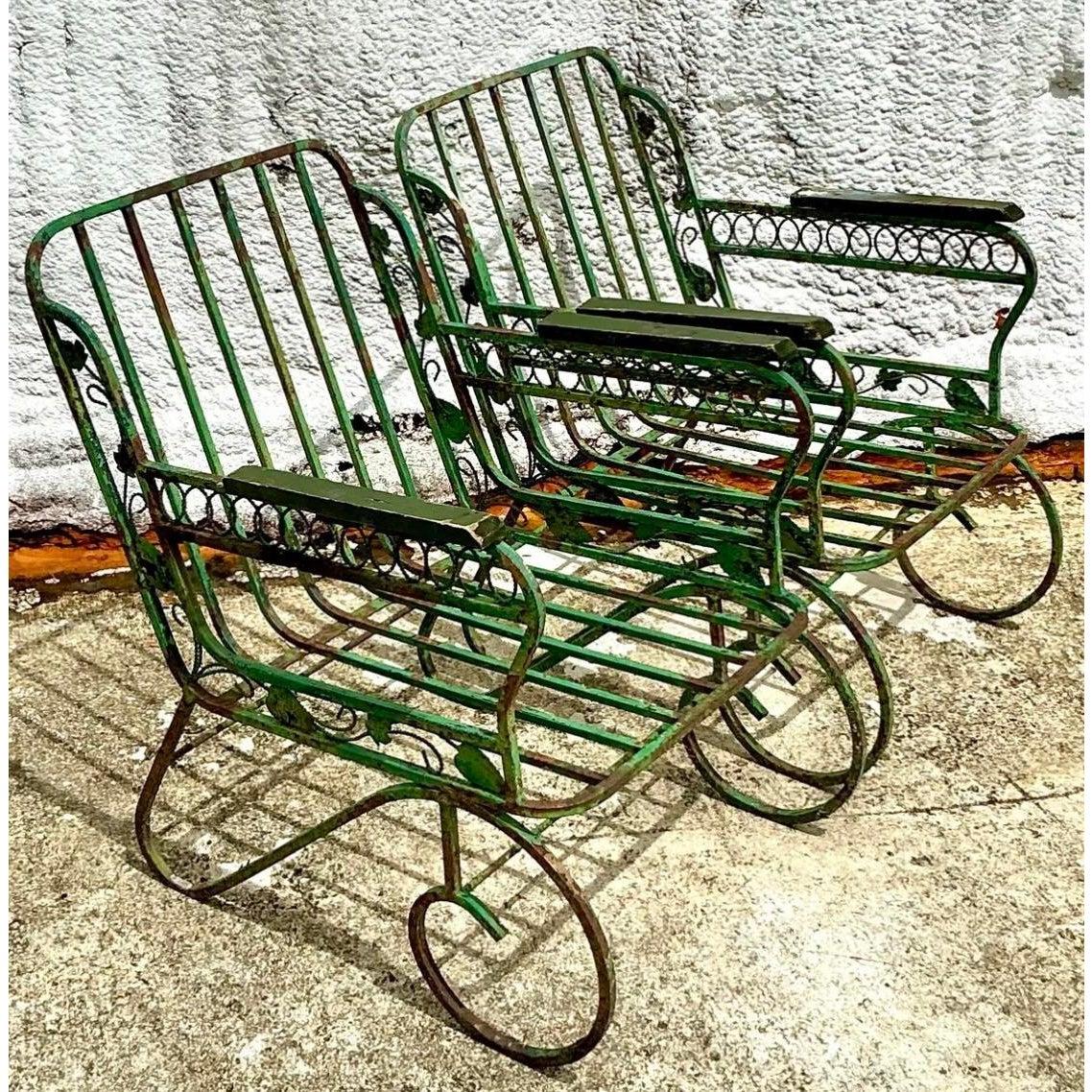 Step into an enchanting garden retreat with this exquisite pair of Vintage Regency Patinated Wrought Iron Lounge Chairs. Evoking a romantic, garden-chic aesthetic, these vintage wrought iron chairs are defined by their charming distressed sage green