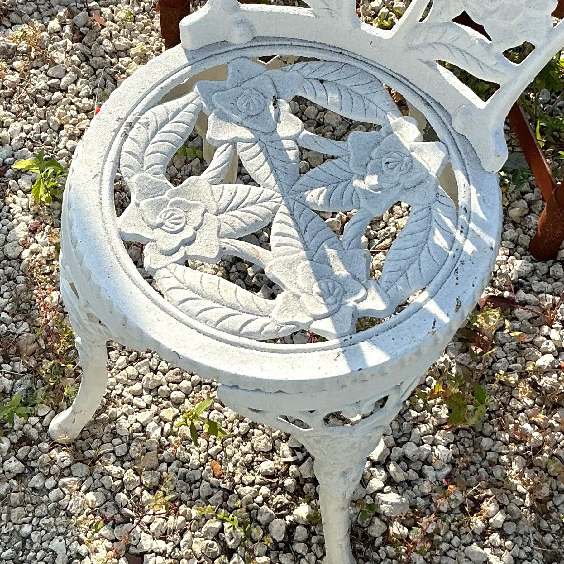 Dieses bezaubernde schmiedeeiserne Set im Regency-Stil besteht aus einem runden Tisch und zwei passenden Stühlen, die alle mit verschlungenen, vom Rosengarten inspirierten Designs versehen sind. Der Tisch ist mit einem verschnörkelten Rosenmotiv auf
