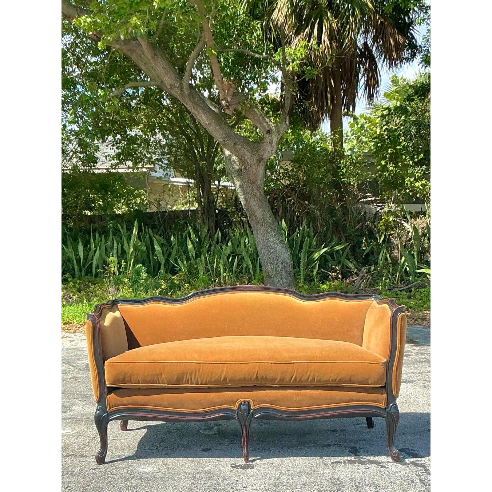 Questo raffinato divanetto vintage in stile Luigi XV incarna un'eleganza senza tempo grazie alla sua silhouette graziosamente curva e alla lussuosa tappezzeria in velluto color senape. La cornice in legno ornatamente intagliata presenta una finitura