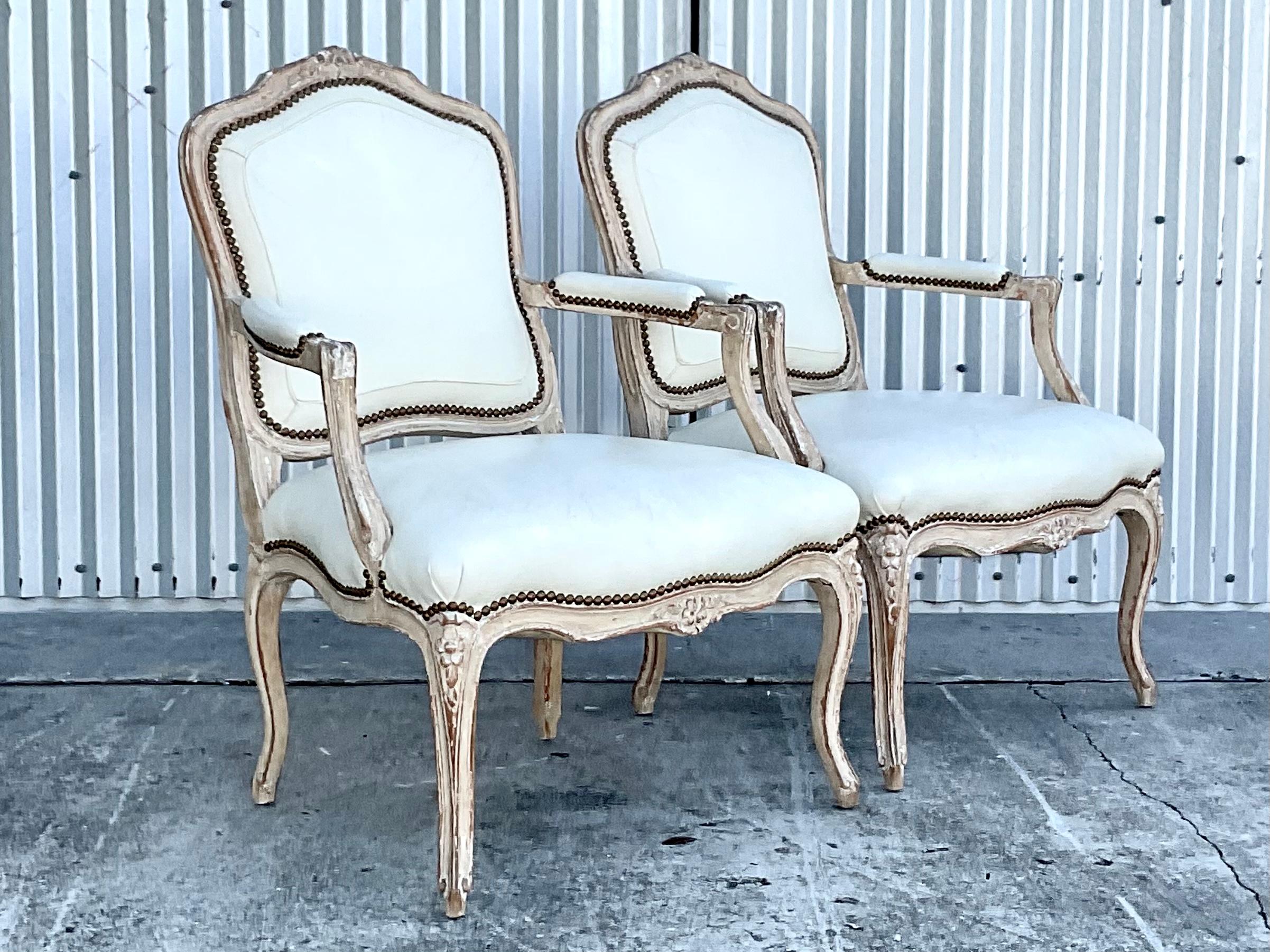 Incredible pair of vintage Regency Bergere chairs. Beautiful cream colored leather with lots of seam detail and brass tacks. Shantung silk back panels and a cerused finish wood frame. Acquired from a Palm Beach estate.