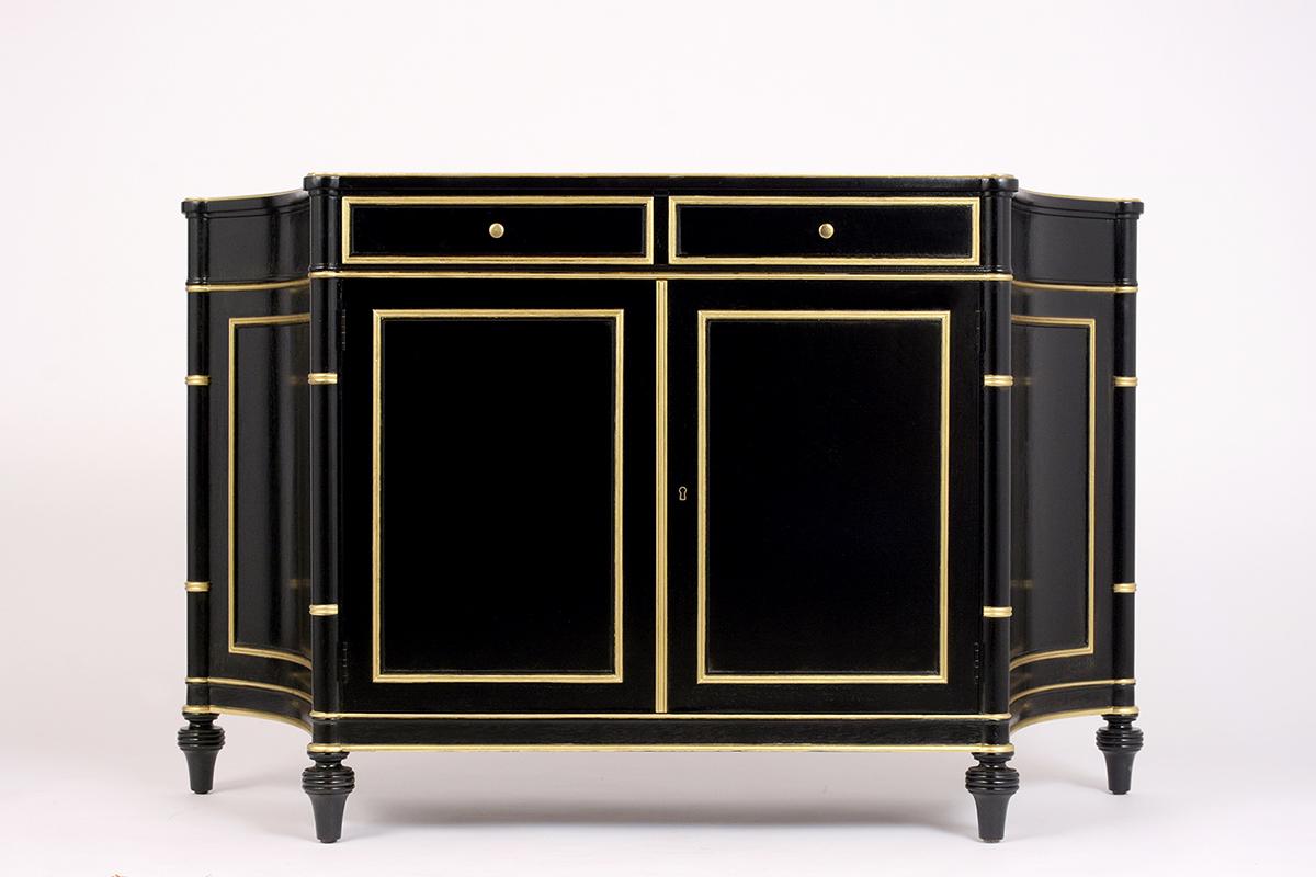 This vintage Regency style ebonized sideboard has been restored and finished in a black and gilt accent combination with a lacquered finish. The sideboard has a wooden top with curved sides, two center drawers with brass knobs, and two large doors