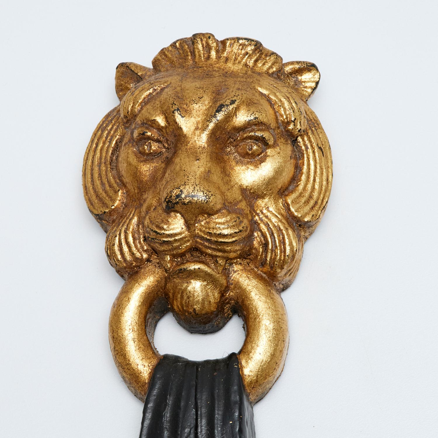 20e s., une paire d'appliques murales vintage en bois et métal doré et noir présentant d'élégants motifs de têtes de lion dans la partie supérieure. Les appliques sont fabriquées dans un style classique, les têtes de lion tenant des anneaux dans