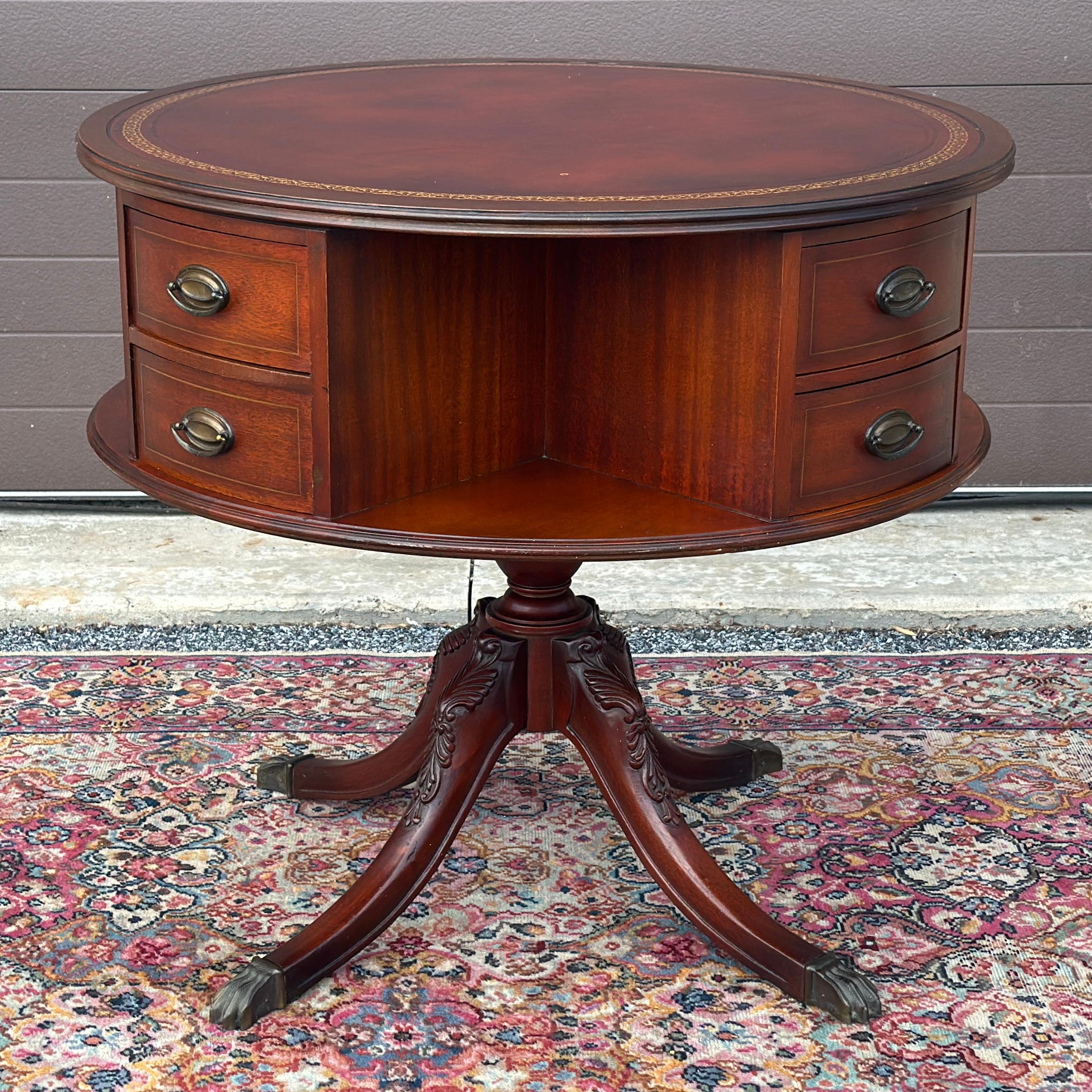 A splendid Regency-style mahogany drum table with tooled leather top above rotating drum of eight drawers and four open shelves all on a pedestal base with carved mahogany legs and brass capped feet. The center drum spins to access any of the