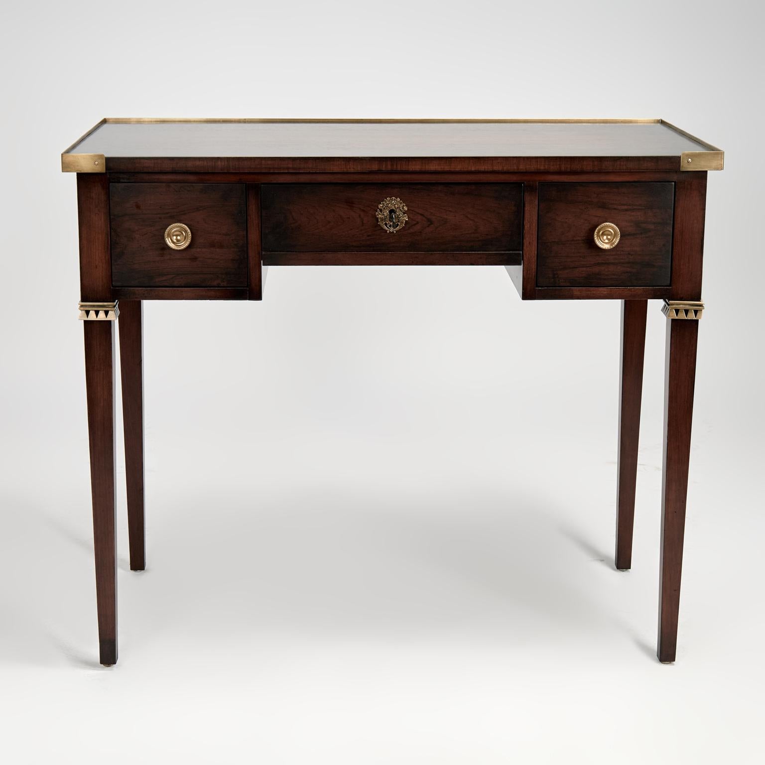 Handsome mid century desk crafted in rosewood in a sleek modern form having a brass banded case with three drawers and brass hardware on elegant tapered legs with brass cuffs. Signed Baker on a silver label in a drawer.

Knee space measures H: 24 W: