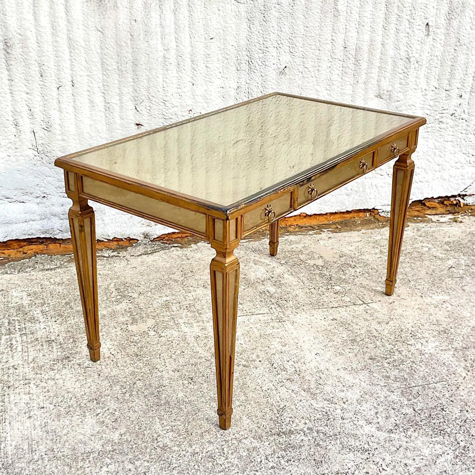 A stunning vintage Regency Writing desk. Made by the iconic Theodore Alexander. A chic Eglomise glass top with a gilt and silvered frame. Signed on the drawer interior. Acquired from a Palm Beach estate.
