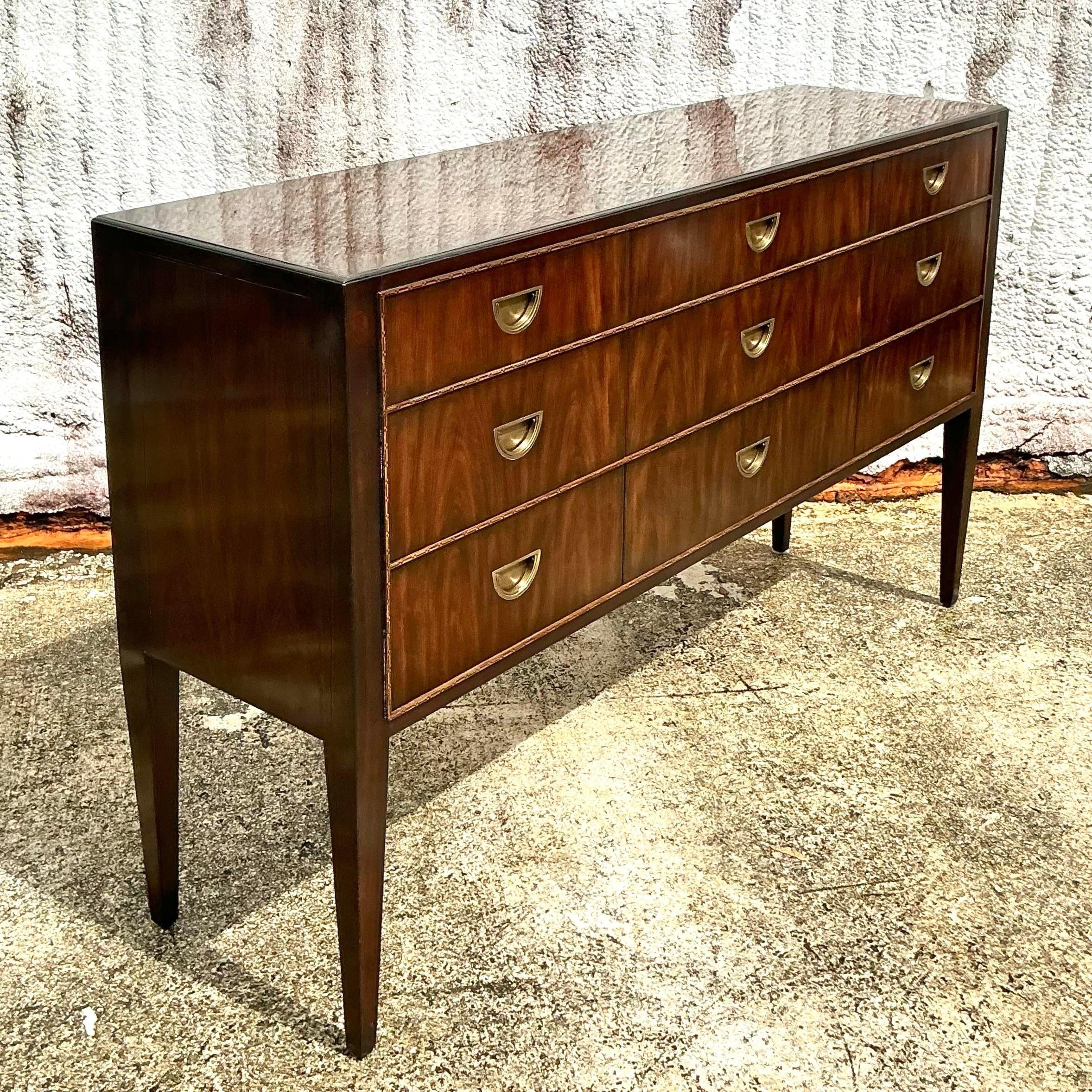 Impressively crafted and full of regal elegance, this vintage Regency Theodore Alexander flame mahogany credenza is a masterpiece of luxury. The rich flame mahogany veneer showcases stunning natural patterns, while the credenza’s timeless design