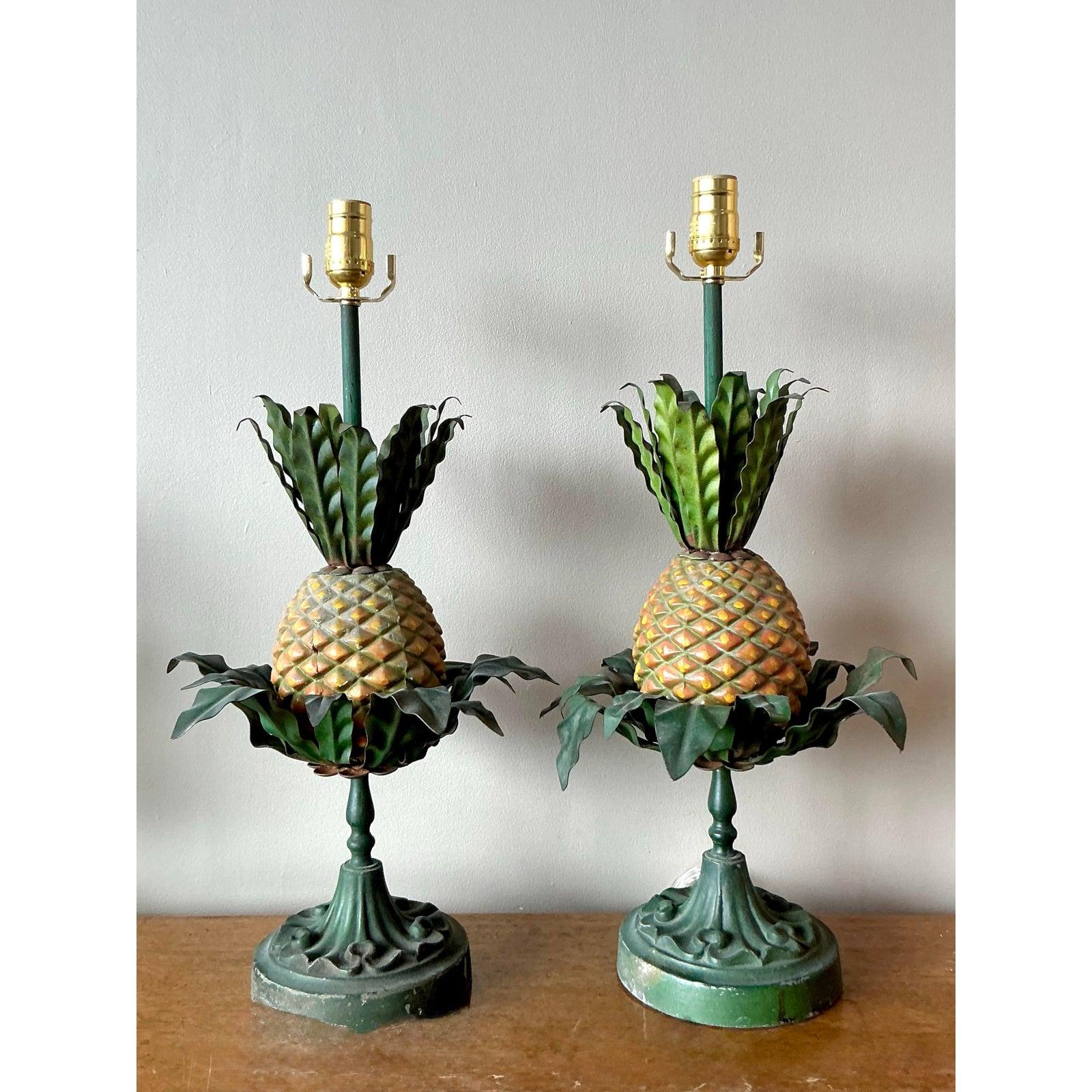 Illuminate your interior with the welcoming spirit of this exquisite pair of vintage pineapple lamps. A quintessential symbol of hospitality, each lamp is masterfully crafted from painted metal (tole), featuring sculptural green leaves that burst