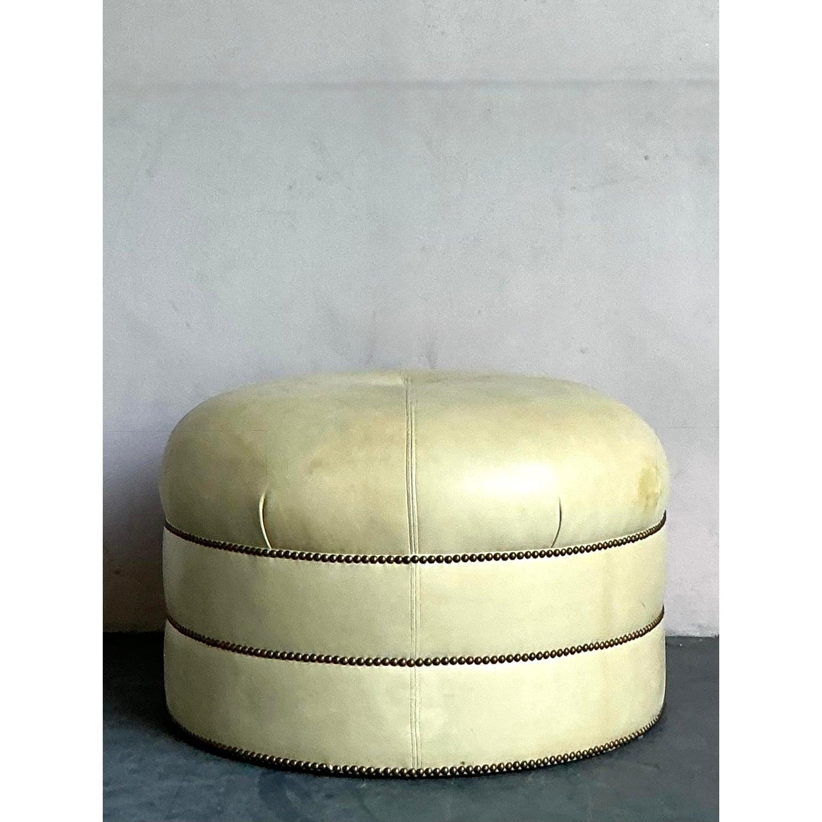 Anchor your living space with this substantial and sophisticated round tufted ottoman. Upholstered in a soft, creamy beige leather or microsuede, this piece exudes a timeless elegance reminiscent of the Art Deco and Hollywood Regency eras. The