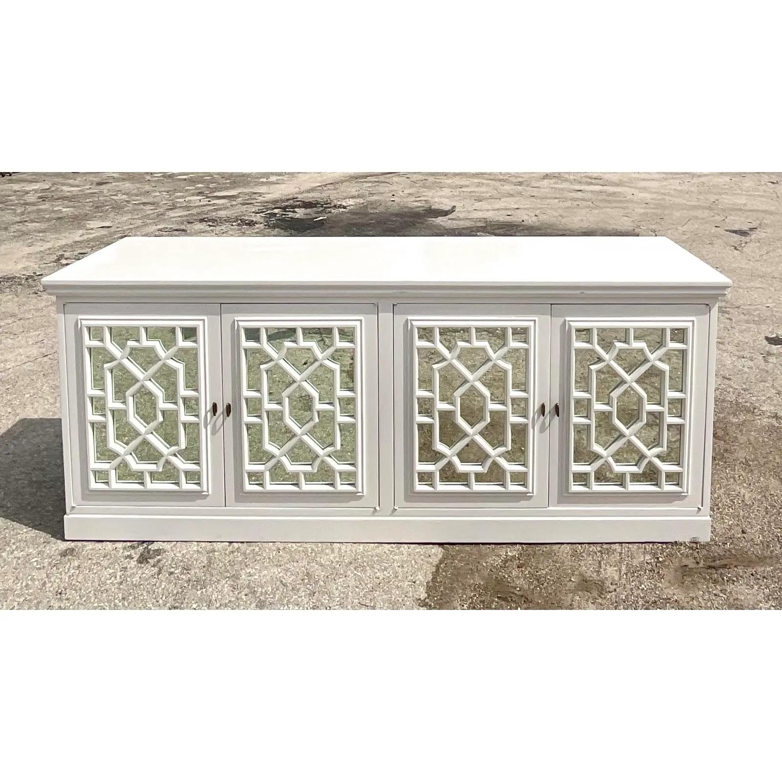 Fantastic vintage Regency white lacquer credenza. Beautiful fretwork mill work offered mirrored doors. Lots of great storage below. Acquired from a Palm Beach estate.